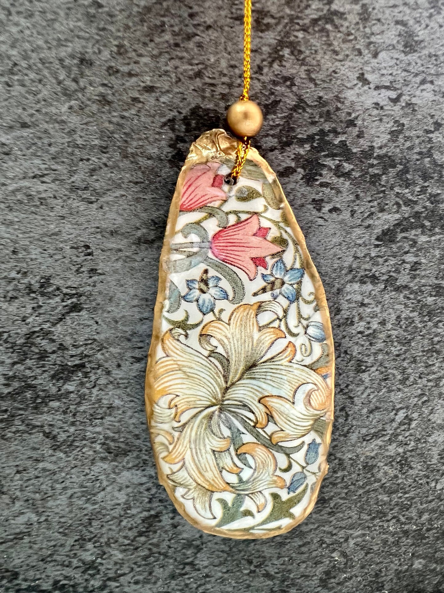 Handmade Dorset oyster shell hanging ornaments featuring William Morris inspired Golden Lily and Granville floral designs in soft green, blush pink and gold tones. Natural oyster shells finished with liquid gold leaf edging and sealed in glossy resin. Decorative hanging ornaments with gold cord and bead detail, suitable for luxury Christmas décor, coastal interiors, cottagecore styling or elegant year-round home decoration.