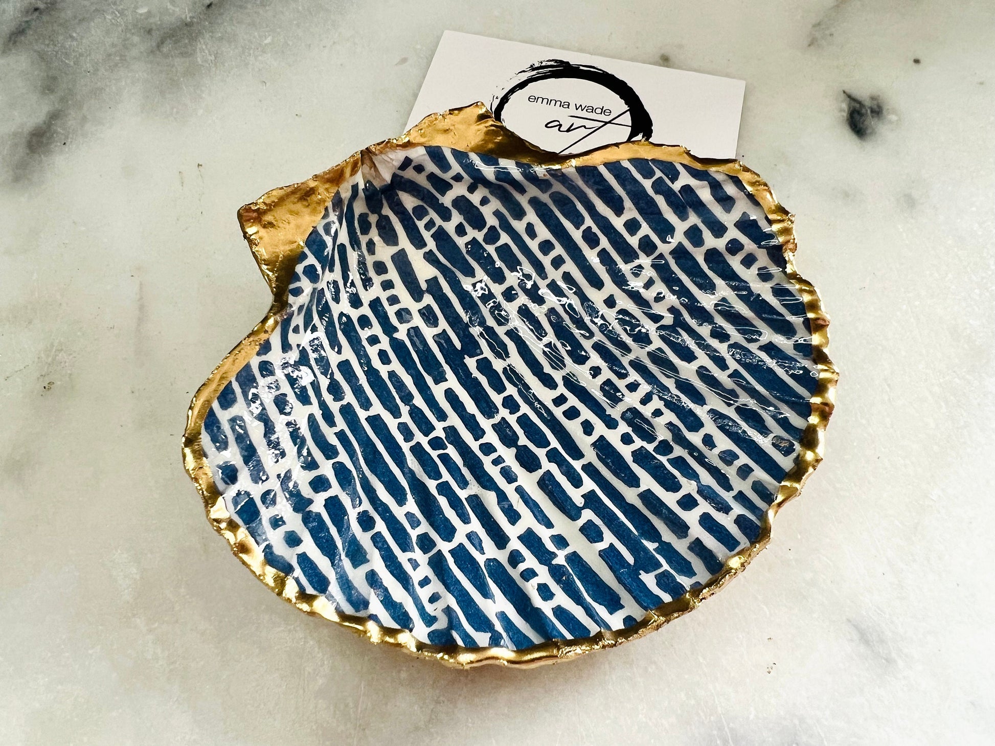 Handmade blue and white scallop shell trinket dish with gold leaf edging, crafted from a genuine Dorset shell and sealed with glossy resin. Coastal ring dish and jewellery holder featuring elegant blue line design, displayed in gift packaging. Artisan shell decor handmade in Surrey, perfect for coastal home styling, wedding gifts or nautical themed interiors.