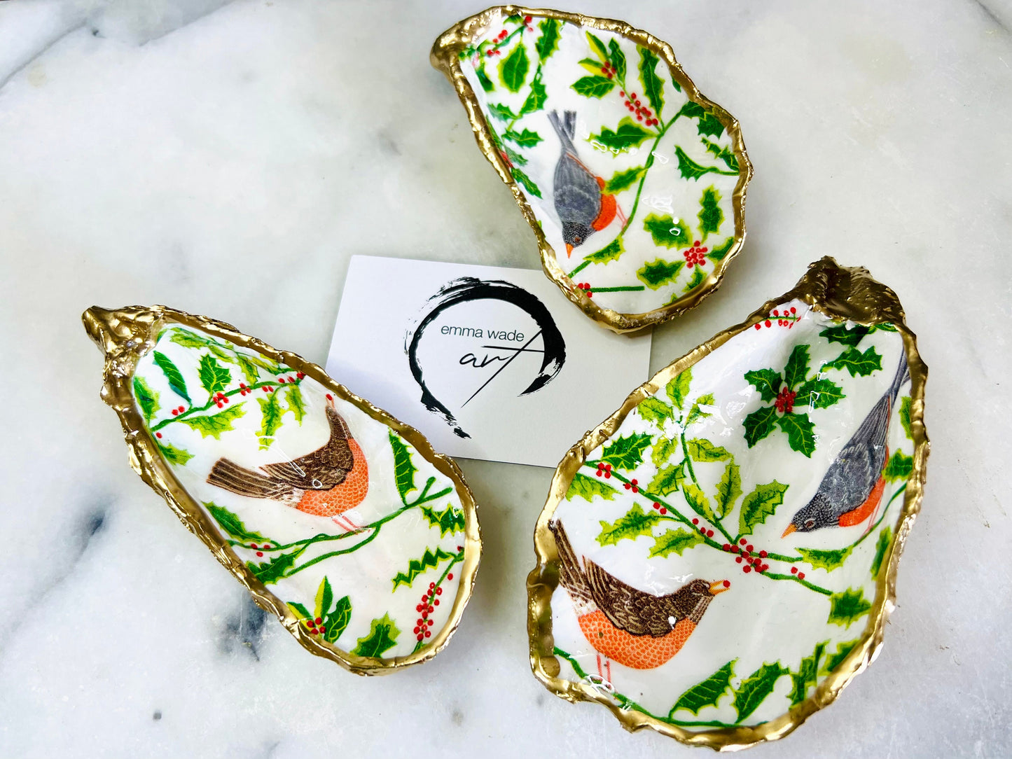 Handmade Dorset oyster shell Christmas ornament featuring red and orange winter birds perched amongst festive green foliage and berries. Coastal oyster shell trinket dish with hand applied gold leaf edging and glossy resin finish, styled as luxury Christmas décor. Sustainable handcrafted robin-inspired shell decoration available as hanging ornament or jewellery dish, inspired by British winter wildlife and the Dorset coastline.