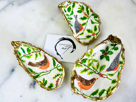 Handmade Dorset oyster shell Christmas ornament featuring red and orange winter birds perched amongst festive green foliage and berries. Coastal oyster shell trinket dish with hand applied gold leaf edging and glossy resin finish, styled as luxury Christmas décor. Sustainable handcrafted robin-inspired shell decoration available as hanging ornament or jewellery dish, inspired by British winter wildlife and the Dorset coastline.