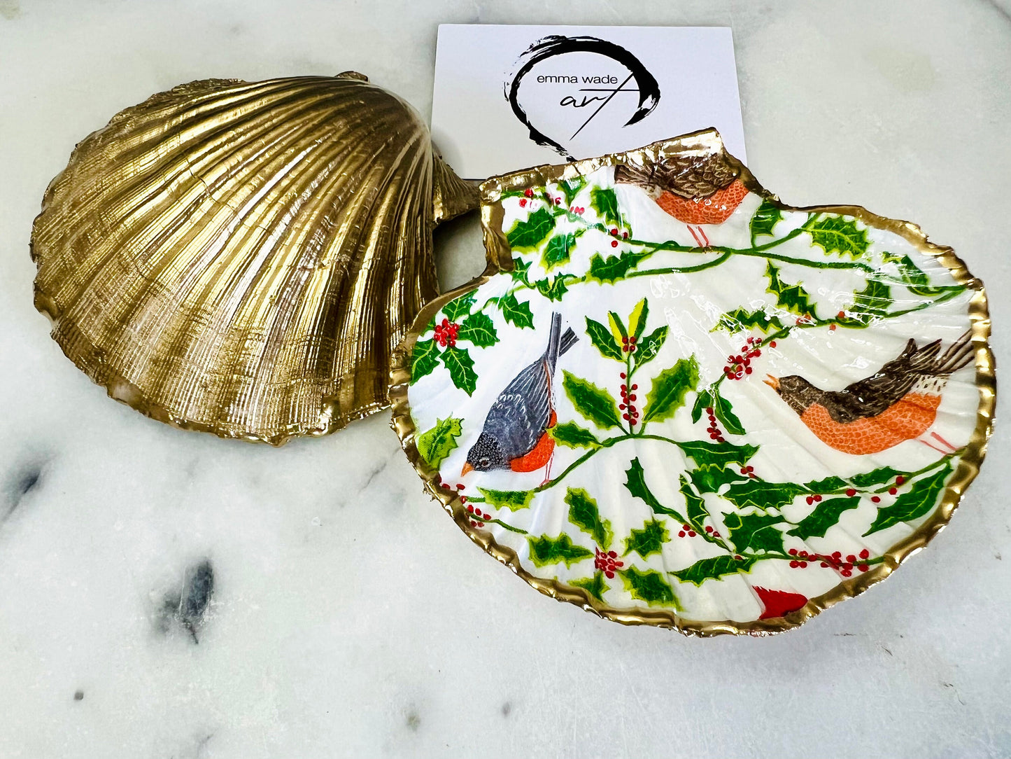 Handmade Dorset scallop shell trinket dish decorated with winter robin and woodland bird illustrations surrounded by festive holly leaves and berries. Natural shell hand finished with liquid gold leaf edging and sealed with glossy resin. Bird décor inspired by coastal cottage interiors and nature styling, suitable as a jewellery dish, ring tray, festive ornament, robin lover gift, winter home décor or Christmas stocking filler.