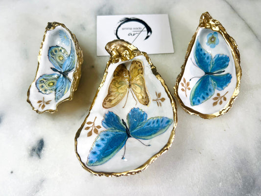Blue yellow green butterfly oyster shell trinket dish handmade from Dorset coast shell, gold leaf gilded rim and back, high gloss resin interior with colourful butterfly design, coastal home decor jewellery dish, ring holder, trinket tray, seaside gift for her, handmade shell decor, luxury coastal accessory, unique artisan gift UK