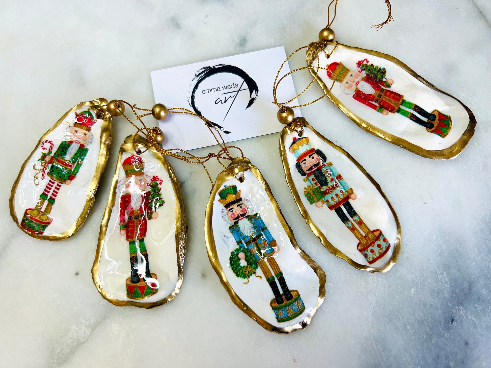 Handmade Nutcracker oyster shell Christmas ornaments with gold gilded edges and glossy resin finish. Traditional festive Nutcracker designs on natural pearl Dorset oyster shells in red, green, aqua, blue and gold tones, styled as luxury coastal Christmas tree decorations.