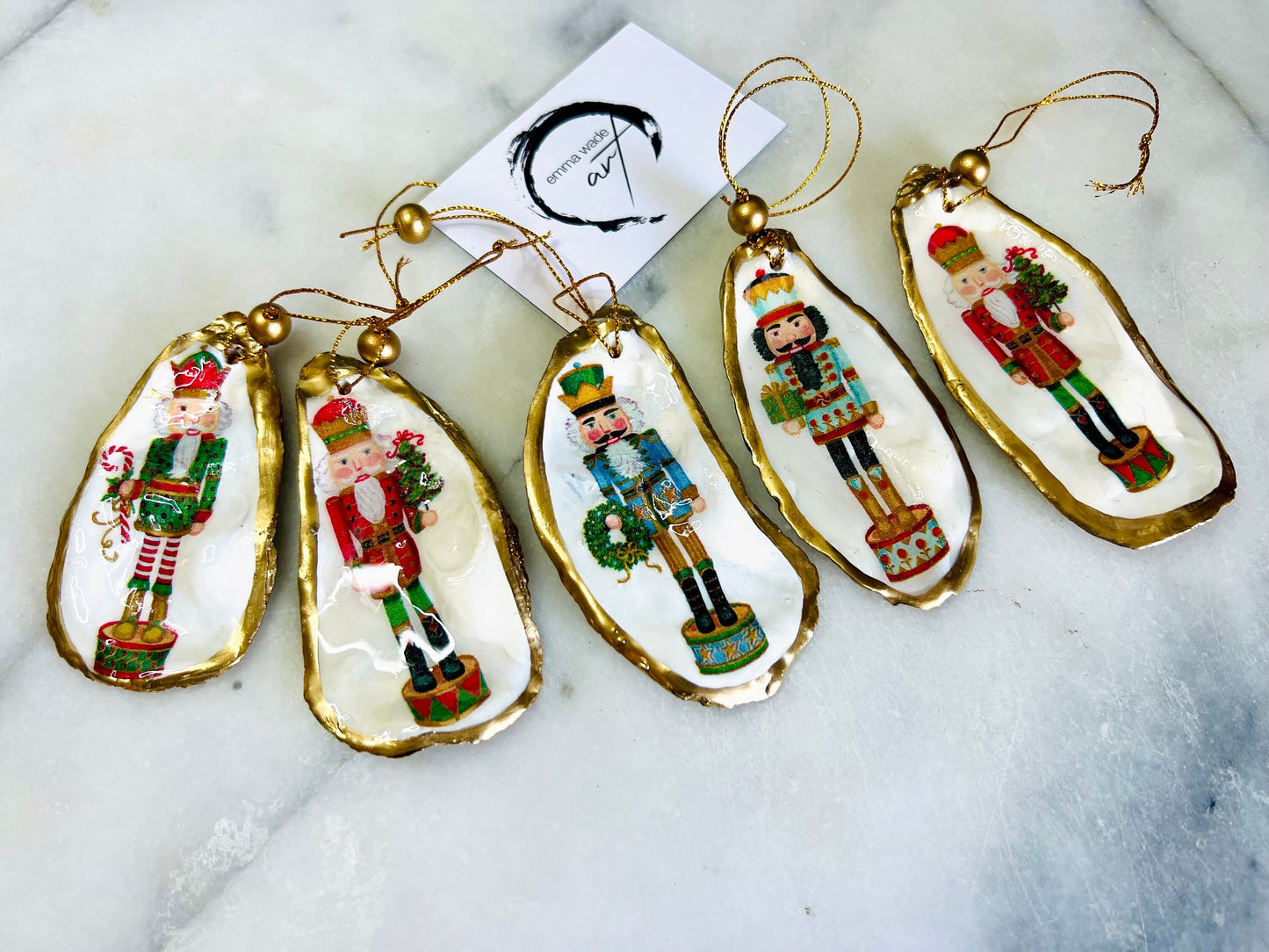 Handmade Nutcracker oyster shell Christmas ornaments with gold gilded edges and glossy resin finish. Traditional festive Nutcracker designs on natural pearl Dorset oyster shells in red, green, aqua, blue and gold tones, styled as luxury coastal Christmas tree decorations.