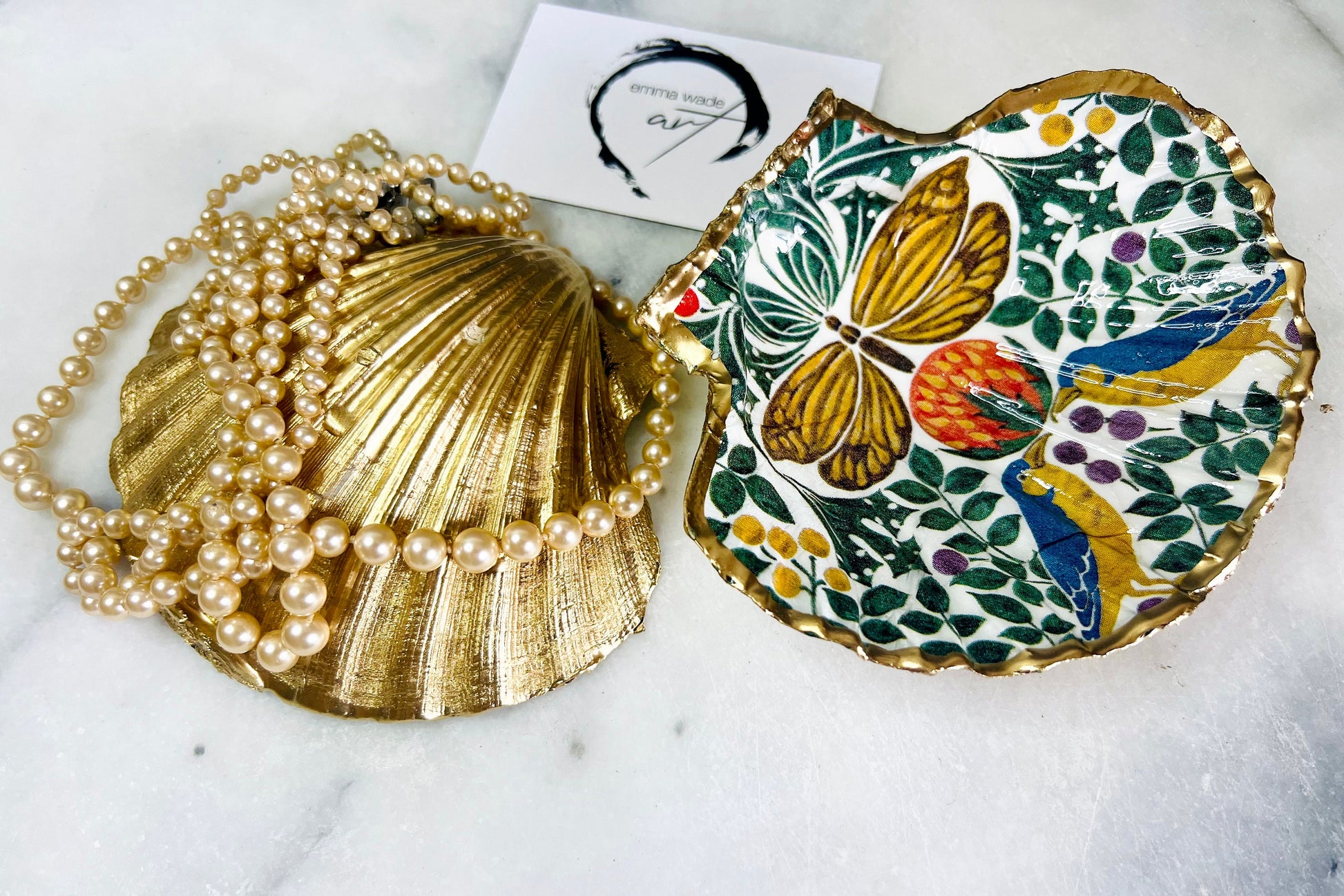 Handmade scallop shell trinket dish featuring a bird and butterfly design, finished with liquid gold leaf and a glossy resin seal. Shown as a decorative jewellery tray on a light background, perfect for holding rings, earrings, and small keepsakes. Crafted from natural Dorset shells, each piece is unique and makes a beautiful coastal-inspired gift for a dressing table, bedside, or bathroom decor.