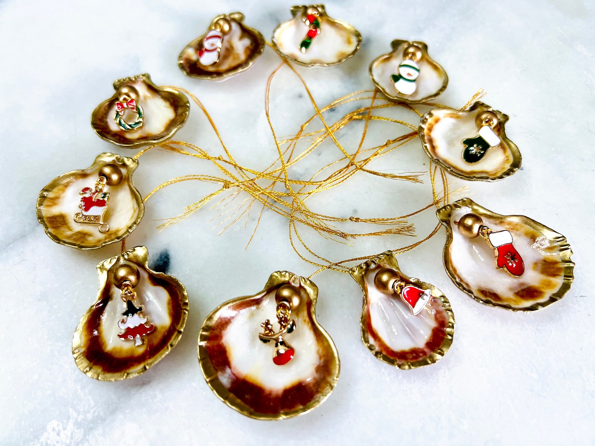Handmade scallop shell Christmas ornaments with gold leaf edging and enamel charms, natural pearl shell decorations, Dorset shell baubles, festive tree decorations, stocking filler gifts, coastal Christmas decor, small hanging ornaments with gold string, unique handmade shell keepsake, wreath sleigh tree reindeer bell penguin charms, luxury Christmas gift idea