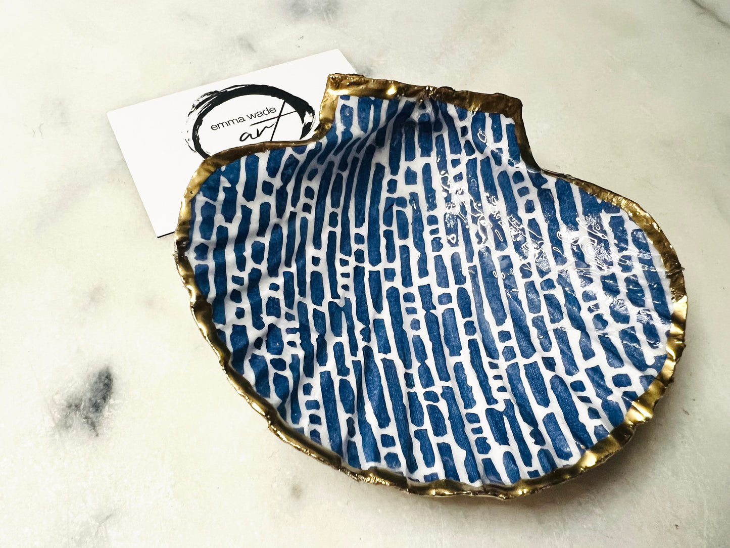 Handmade blue and white scallop shell trinket dish with gold leaf edging, crafted from a genuine Dorset shell and sealed with glossy resin. Coastal ring dish and jewellery holder featuring elegant blue line design, displayed in gift packaging. Artisan shell decor handmade in Surrey, perfect for coastal home styling, wedding gifts or nautical themed interiors.