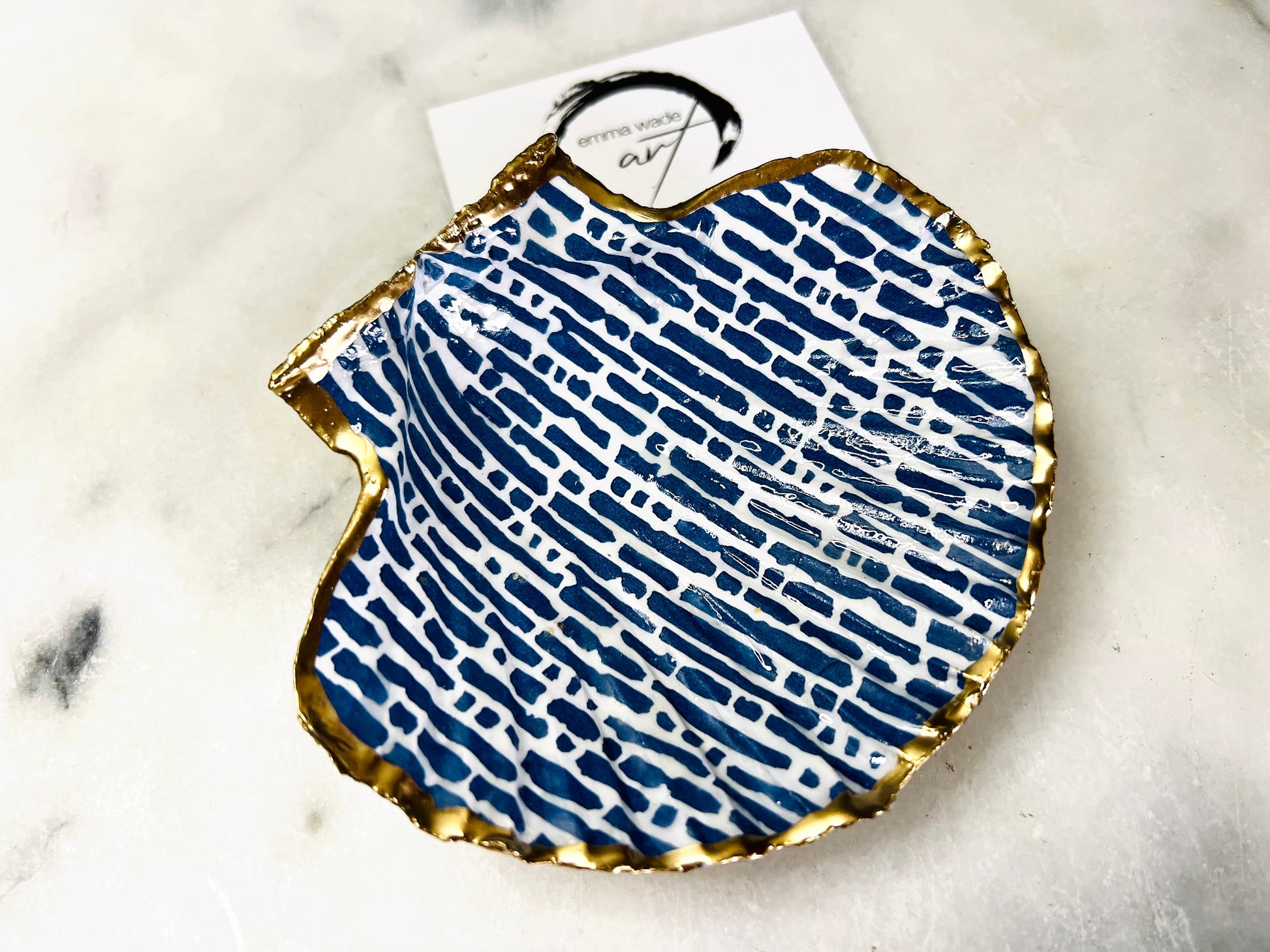 Handmade blue and white scallop shell trinket dish with gold leaf edging, crafted from a genuine Dorset shell and sealed with glossy resin. Coastal ring dish and jewellery holder featuring elegant blue line design, displayed in gift packaging. Artisan shell decor handmade in Surrey, perfect for coastal home styling, wedding gifts or nautical themed interiors.