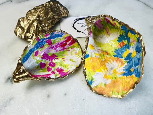 Handmade Dorset oyster shell trinket dish featuring colourful floral artwork in pink, yellow, orange, and blue tones with genuine gold leaf edging and glossy resin finish. Coastal jewellery holder and vibrant floral home décor gift.