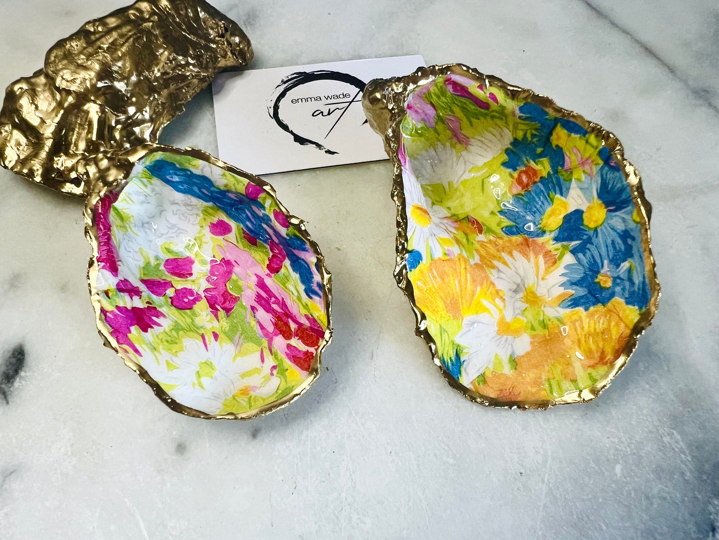 Handmade Dorset oyster shell trinket dish featuring colourful floral artwork in pink, yellow, orange, and blue tones with genuine gold leaf edging and glossy resin finish. Coastal jewellery holder and vibrant floral home décor gift.