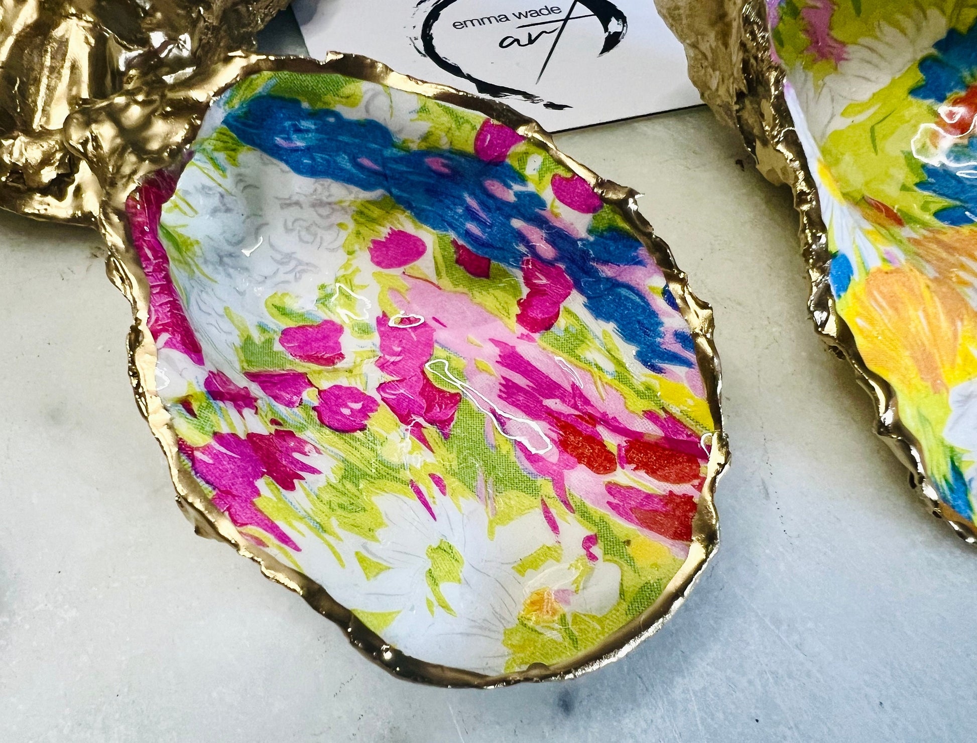 Handmade Dorset oyster shell trinket dish featuring colourful floral artwork in pink, yellow, orange, and blue tones with genuine gold leaf edging and glossy resin finish. Coastal jewellery holder and vibrant floral home décor gift.