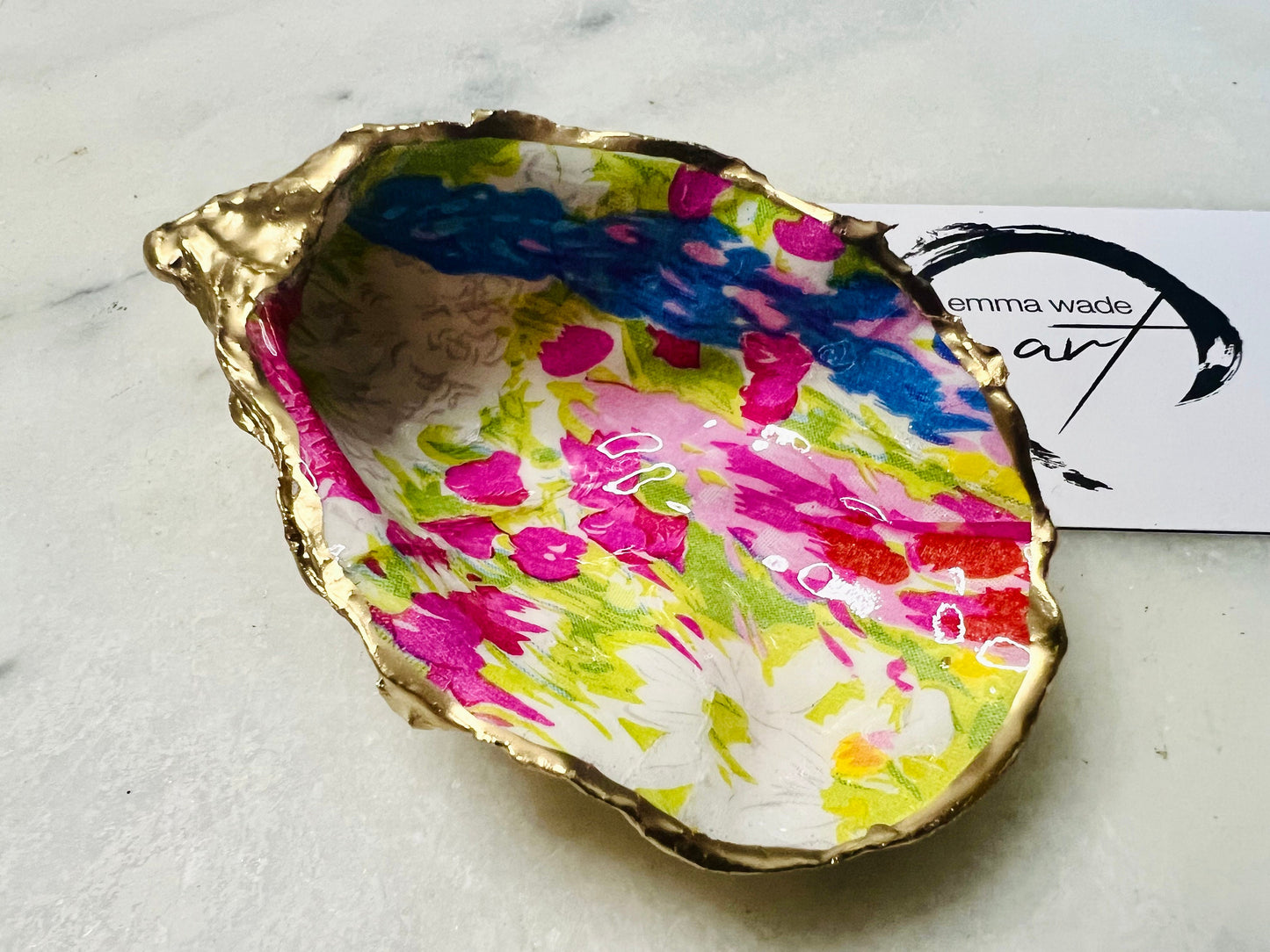 Handmade Dorset oyster shell trinket dish featuring colourful floral artwork in pink, yellow, orange, and blue tones with genuine gold leaf edging and glossy resin finish. Coastal jewellery holder and vibrant floral home décor gift.