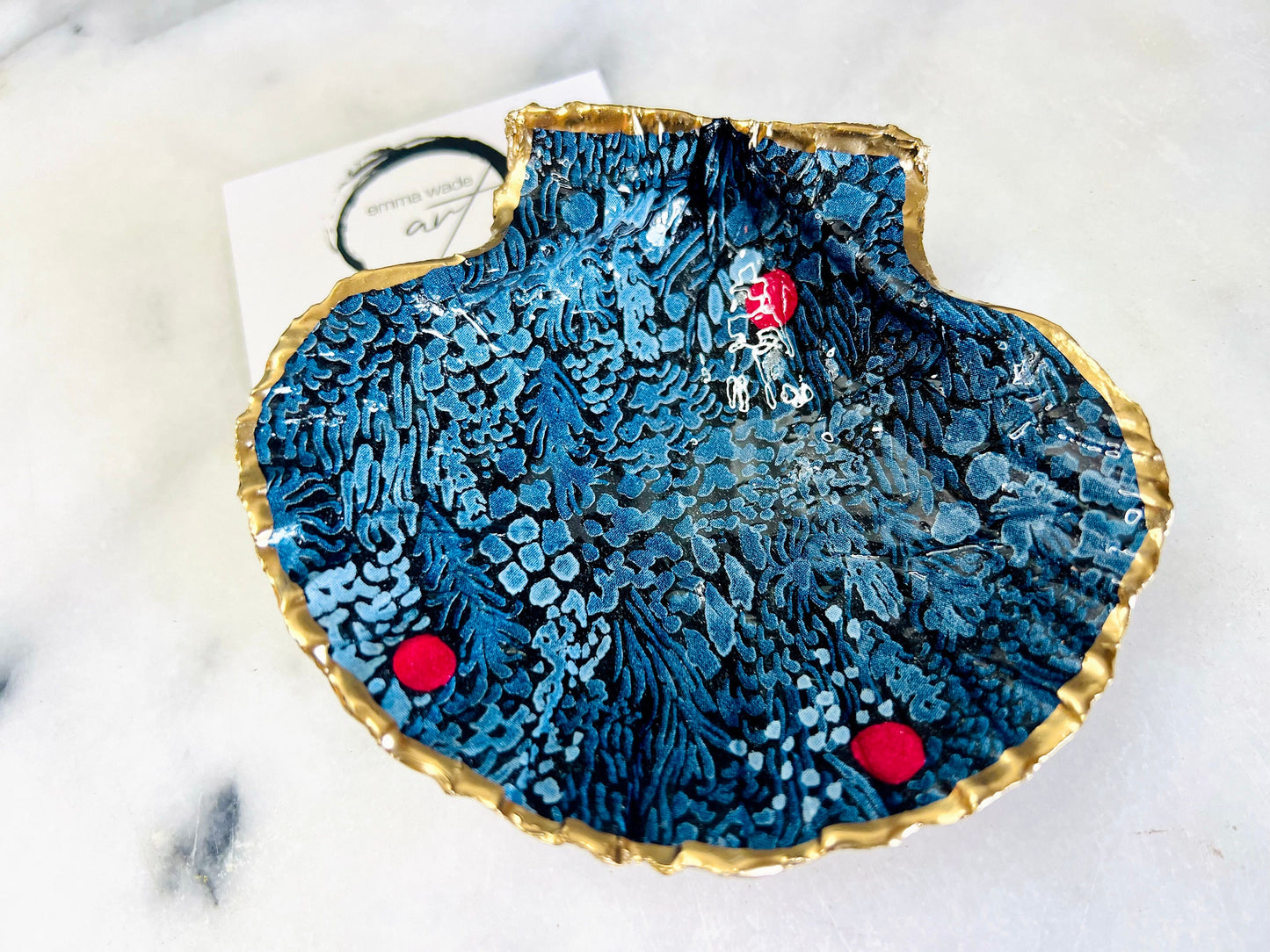 Handmade Marimekko inspired scallop shell trinket dish featuring bold Scandinavian floral design in deep blue with red accents. Natural Dorset scallop shell hand gilded with liquid gold leaf edging and sealed with glossy resin for a luxurious shine. Coastal home décor suitable as a jewellery dish, ring tray, trinket holder, wedding gift, bathroom décor or modern Nordic inspired shelf styling. Unique handcrafted shell décor inspired by botanical Scandinavian design.