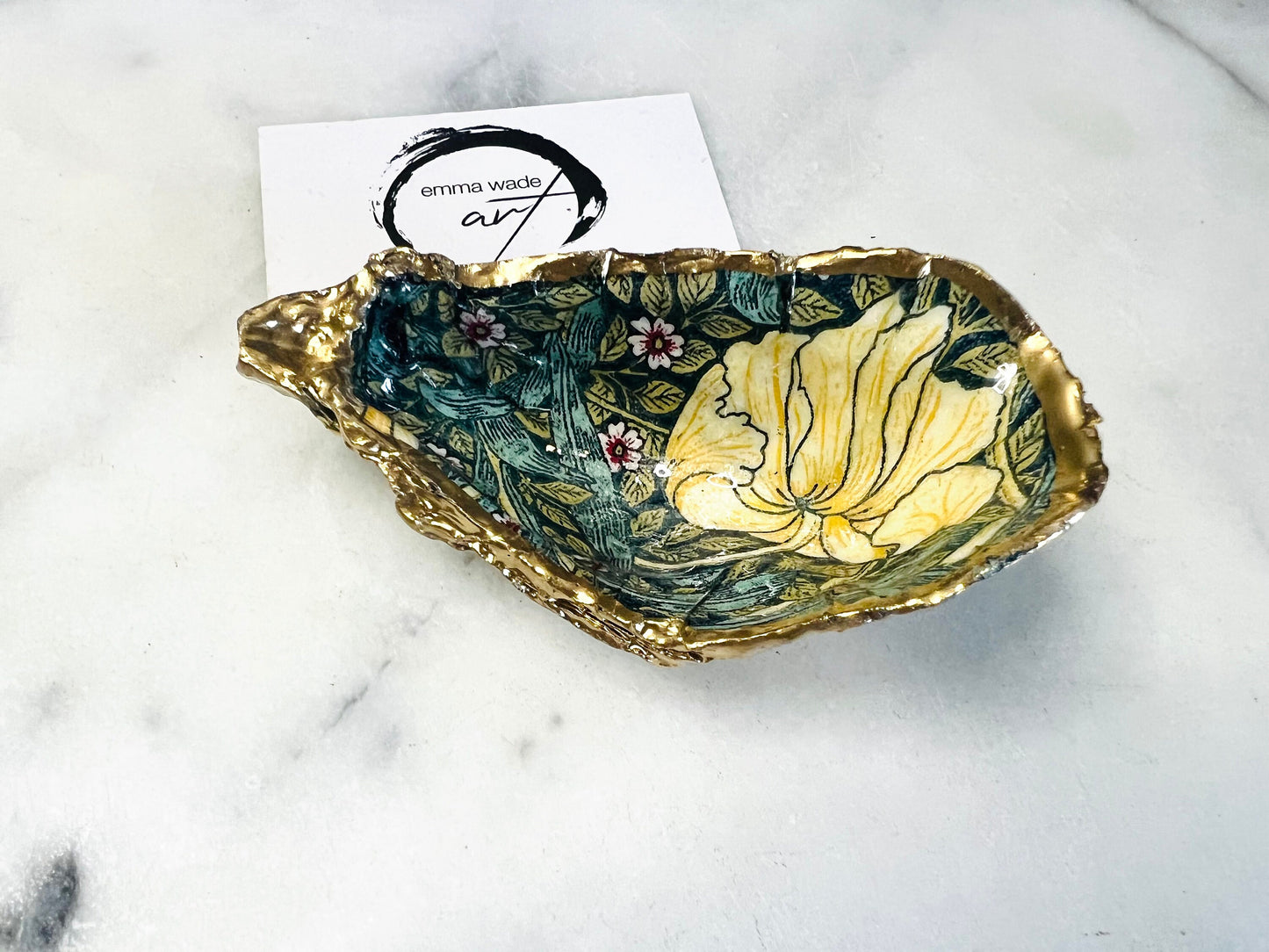 William Morris Golden Green Pimpernel oyster shell ring dish with gold leaf edge. A unique shell ring holder, ring tray, and jewellery organiser for rings, earrings, or cufflinks. Each shell features an art inspired floral design and is individually handmade from Dorset shells. Perfect as a trinket dish for bedside or dressing table storage. A thoughtful gift for weddings, anniversaries, birthdays, bridesmaids, or Christmas. A sustainable decorative keepsake for any jewellery lover.