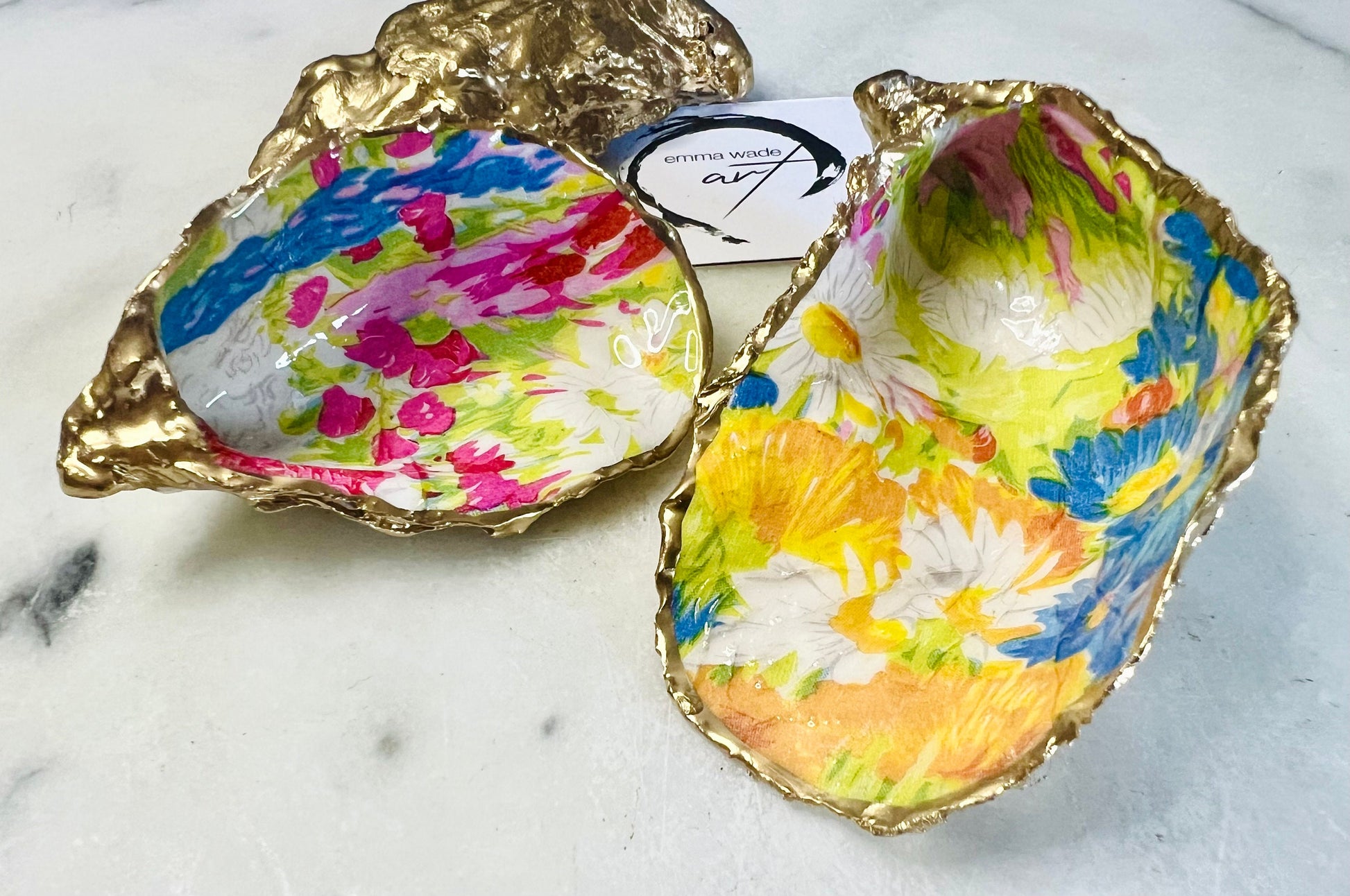 Handmade Dorset oyster shell trinket dish featuring colourful floral artwork in pink, yellow, orange, and blue tones with genuine gold leaf edging and glossy resin finish. Coastal jewellery holder and vibrant floral home décor gift.