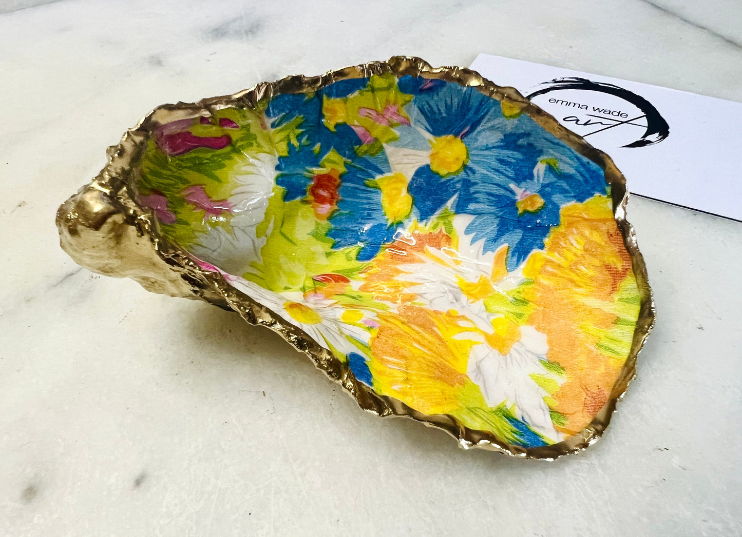 Handmade Dorset oyster shell trinket dish featuring colourful floral artwork in pink, yellow, orange, and blue tones with genuine gold leaf edging and glossy resin finish. Coastal jewellery holder and vibrant floral home décor gift.