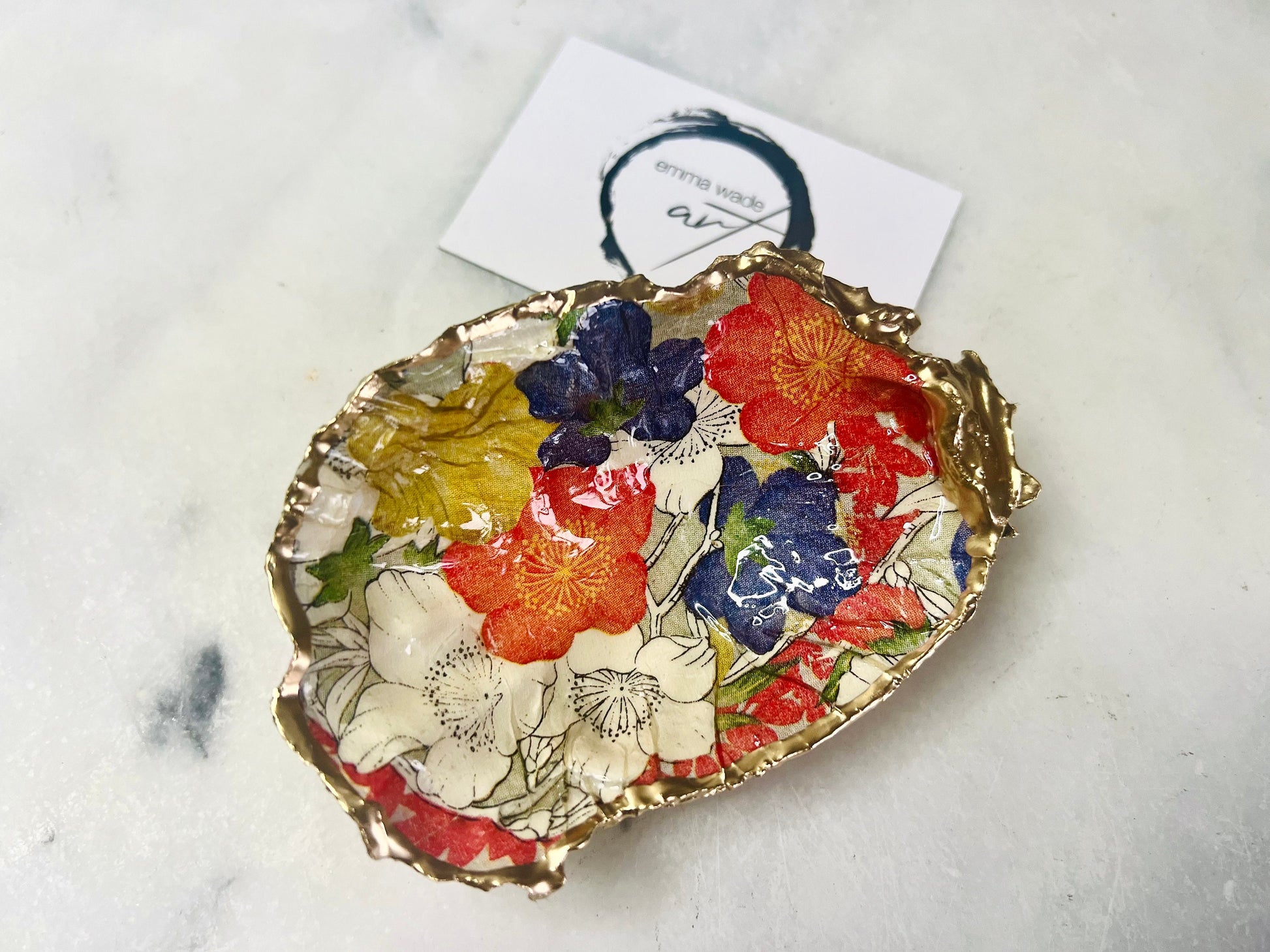 Handmade oyster shell trinket dish featuring a colourful Japanese kimono-style floral design applied with decoupage, finished with hand-gilded gold leaf edges and sealed in glossy clear resin. Natural Dorset oyster shell used as a jewellery dish or ring holder, photographed on a light surface, showcasing the vibrant flowers and luxury gold detailing. Ideal as coastal home decor or a unique handmade gift.