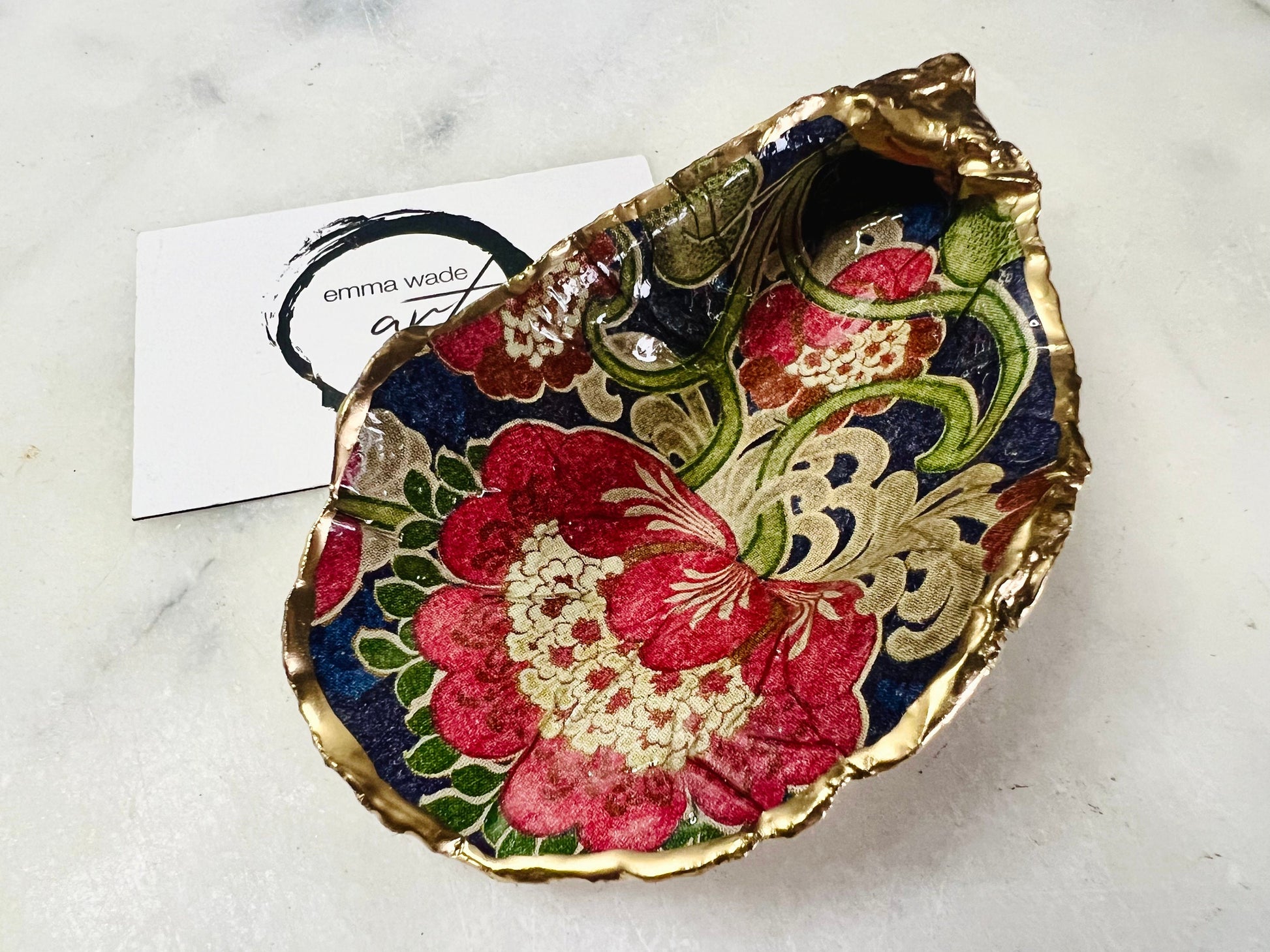 Handmade oyster shell trinket dish featuring a retro floral botanical pattern in pink, red, navy, and olive tones with gold leaf edging and glossy resin finish. Vintage V&A inspired oyster shell jewellery dish styled as coastal cottagecore home décor.