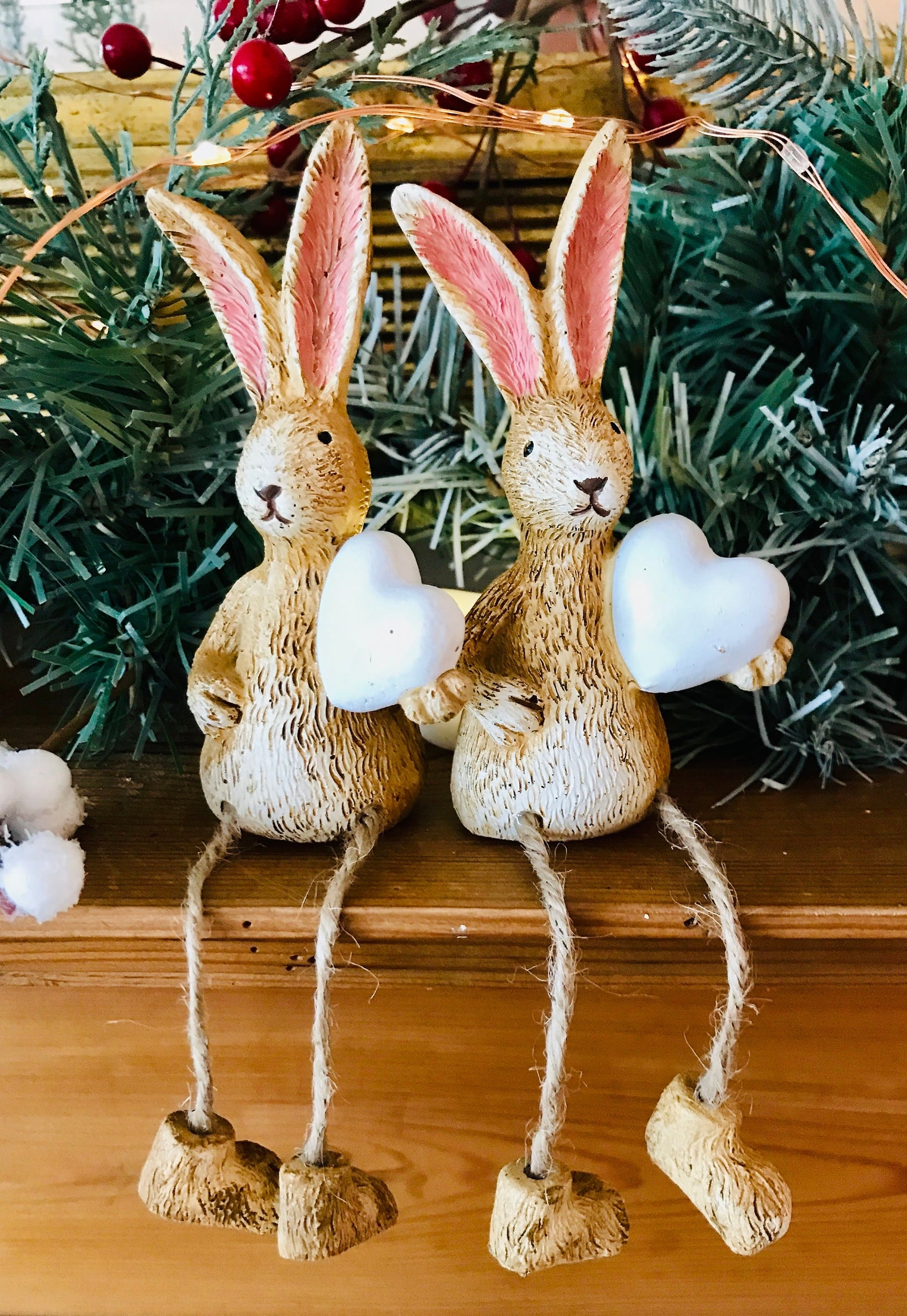 Hand finished rustic bunny shelf sitters holding white wooden hearts, gold and grey rabbit ornaments with pink ears and dangling jute legs, styled on wooden mantlepiece as charming year-round home decor.