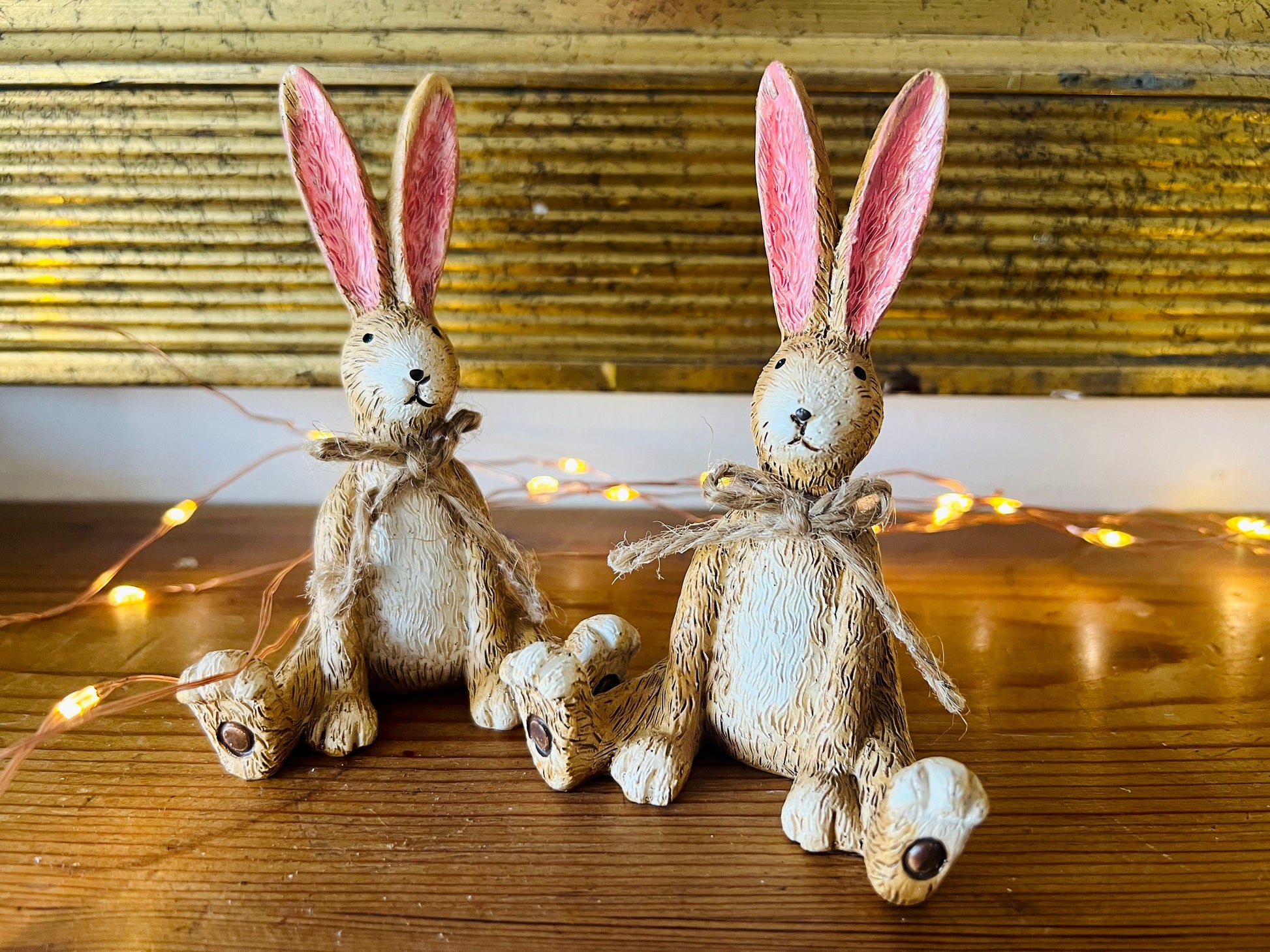 Hand finished brown resin rabbit ornament with rustic jute bow and pink inner ears, seated bunny shelf sitter with detailed textured fur finish. Decorative rabbit figurine styled on a wooden stand against a neutral background. A charming rustic home decor piece ideal for mantel display, nursery styling, cottage interiors or country farmhouse decor. Thoughtful gift for her, new home gift, Mother’s Day present or year round bunny decoration.