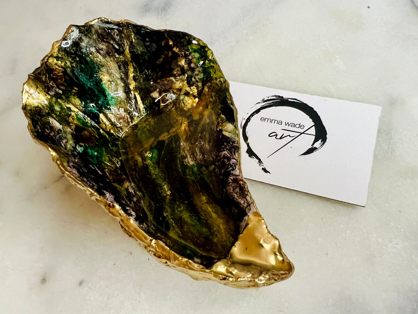 Extra large oyster shell dish with green and gold lagoon design, created using poured acrylic inks and layered resins for a deep ocean effect. Finished with shimmering gold edges, this handmade shell is a unique one-of-a-kind piece of coastal art. Can be used as a jewellery dish, ring holder, trinket tray, or decorative ornament. Also suitable as a serving dish for canapés or chocolates. Inspired by sea caves and lagoons, each shell is natural, rare, and individually crafted.