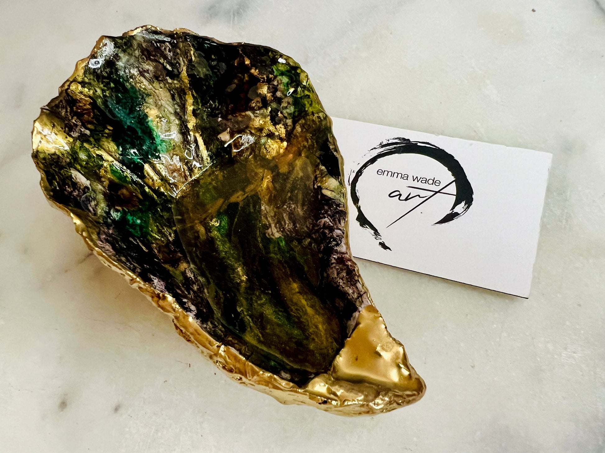 Extra large oyster shell dish with green and gold lagoon design, created using poured acrylic inks and layered resins for a deep ocean effect. Finished with shimmering gold edges, this handmade shell is a unique one-of-a-kind piece of coastal art. Can be used as a jewellery dish, ring holder, trinket tray, or decorative ornament. Also suitable as a serving dish for canapés or chocolates. Inspired by sea caves and lagoons, each shell is natural, rare, and individually crafted.