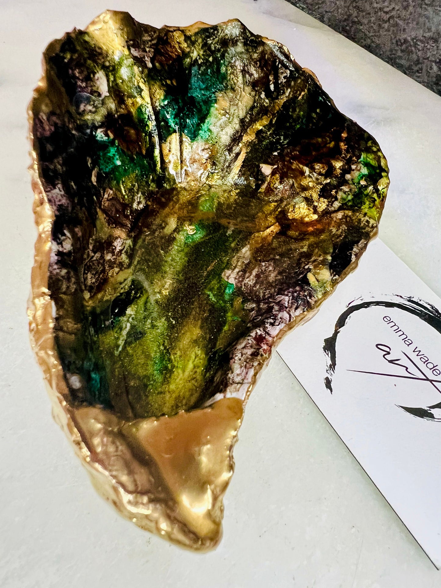 Extra large oyster shell dish with green and gold lagoon design, created using poured acrylic inks and layered resins for a deep ocean effect. Finished with shimmering gold edges, this handmade shell is a unique one-of-a-kind piece of coastal art. Can be used as a jewellery dish, ring holder, trinket tray, or decorative ornament. Also suitable as a serving dish for canapés or chocolates. Inspired by sea caves and lagoons, each shell is natural, rare, and individually crafted.