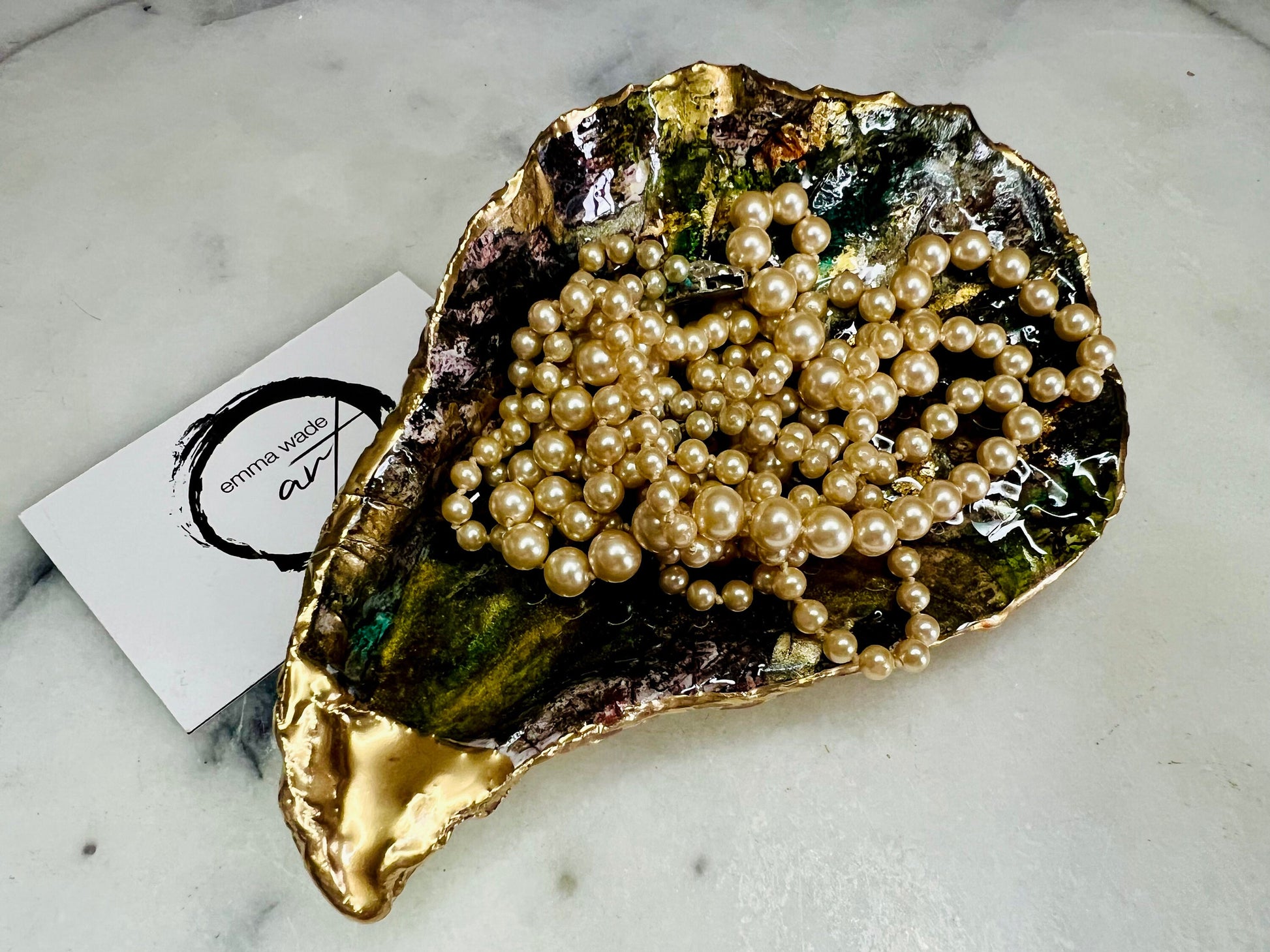 Extra large oyster shell dish with green and gold lagoon design, created using poured acrylic inks and layered resins for a deep ocean effect. Finished with shimmering gold edges, this handmade shell is a unique one-of-a-kind piece of coastal art. Can be used as a jewellery dish, ring holder, trinket tray, or decorative ornament. Also suitable as a serving dish for canapés or chocolates. Inspired by sea caves and lagoons, each shell is natural, rare, and individually crafted.