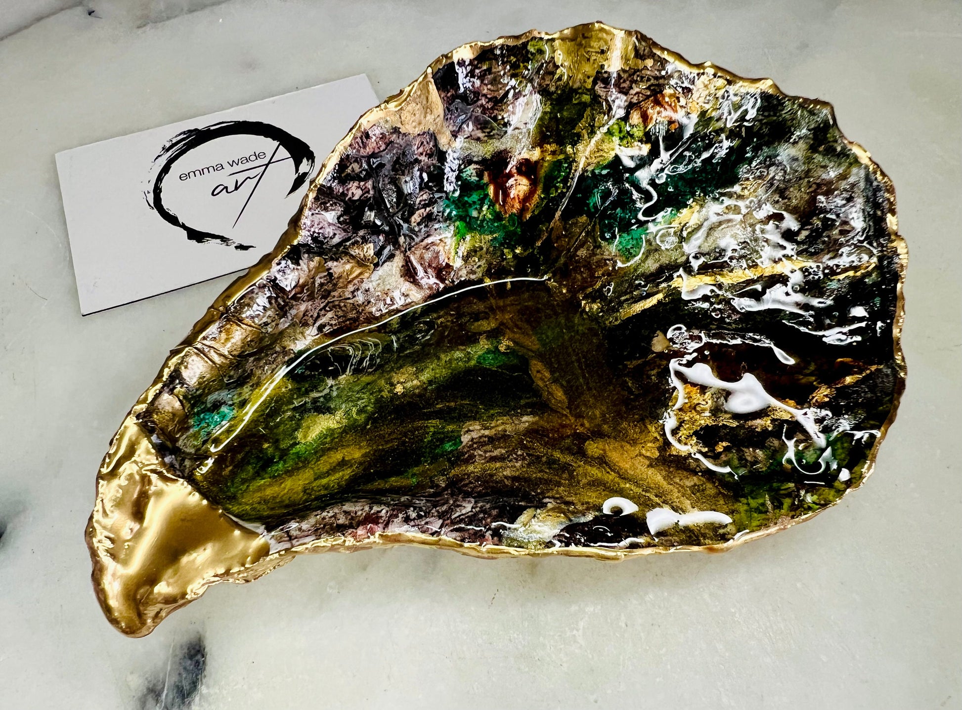Extra large oyster shell dish with green and gold lagoon design, created using poured acrylic inks and layered resins for a deep ocean effect. Finished with shimmering gold edges, this handmade shell is a unique one-of-a-kind piece of coastal art. Can be used as a jewellery dish, ring holder, trinket tray, or decorative ornament. Also suitable as a serving dish for canapés or chocolates. Inspired by sea caves and lagoons, each shell is natural, rare, and individually crafted.