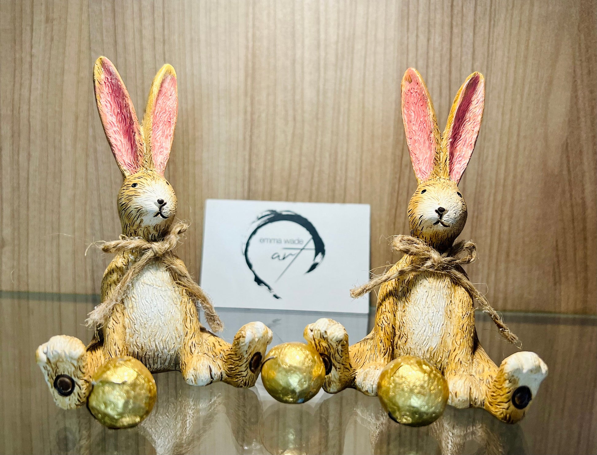 Hand finished brown resin rabbit ornament with rustic jute bow and pink inner ears, seated bunny shelf sitter with detailed textured fur finish. Decorative rabbit figurine styled on a wooden stand against a neutral background. A charming rustic home decor piece ideal for mantel display, nursery styling, cottage interiors or country farmhouse decor. Thoughtful gift for her, new home gift, Mother’s Day present or year round bunny decoration.