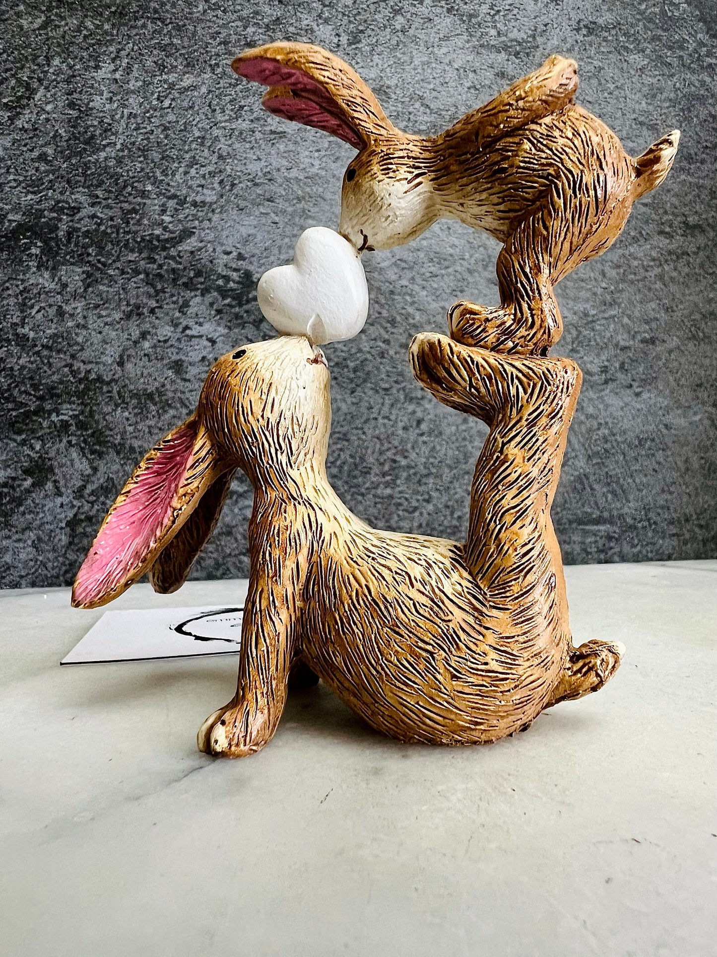 Hand finished brown polyresin bunny and baby rabbit ornament, showing a larger rabbit balancing a baby bunny above with a white heart between them. Rustic textured rabbit figure with pink inner ears, suitable for Christmas shelf decor, mantel styling, rabbit lover gifts and year-round home decoration.