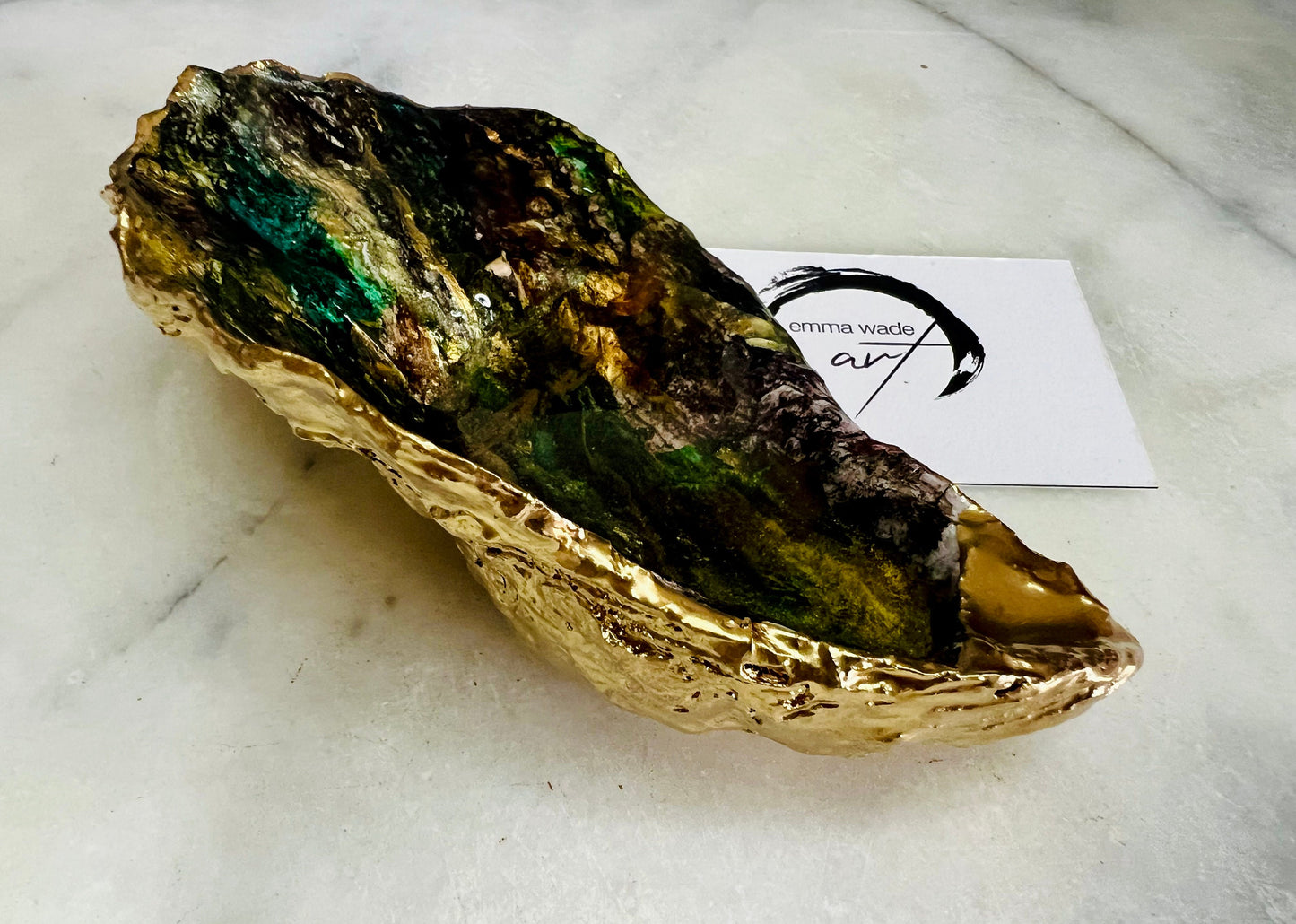 Extra large oyster shell dish with green and gold lagoon design, created using poured acrylic inks and layered resins for a deep ocean effect. Finished with shimmering gold edges, this handmade shell is a unique one-of-a-kind piece of coastal art. Can be used as a jewellery dish, ring holder, trinket tray, or decorative ornament. Also suitable as a serving dish for canapés or chocolates. Inspired by sea caves and lagoons, each shell is natural, rare, and individually crafted.