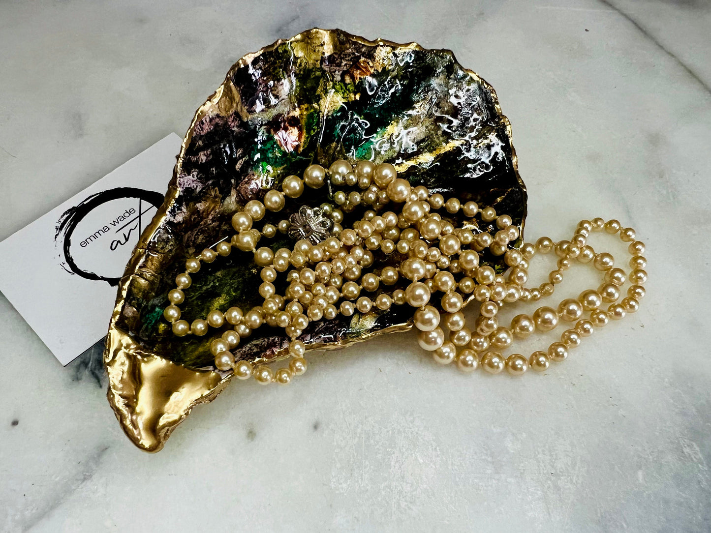 Extra large oyster shell dish with green and gold lagoon design, created using poured acrylic inks and layered resins for a deep ocean effect. Finished with shimmering gold edges, this handmade shell is a unique one-of-a-kind piece of coastal art. Can be used as a jewellery dish, ring holder, trinket tray, or decorative ornament. Also suitable as a serving dish for canapés or chocolates. Inspired by sea caves and lagoons, each shell is natural, rare, and individually crafted.