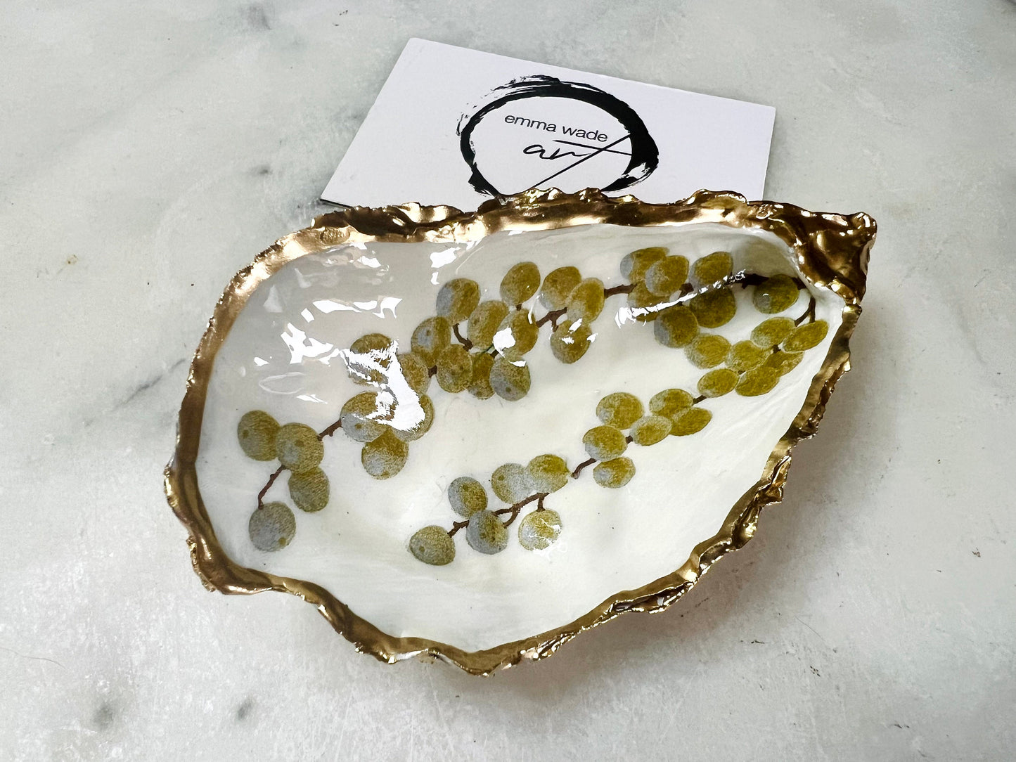 Handmade Dorset oyster shell dish with a gold and white berries design, gilded with liquid gold leaf on the rim and back, and sealed in crystal-clear resin for a glossy shine. Each oyster shell jewellery dish is unique, perfect as a ring holder, trinket tray, or organiser for earrings, cufflinks, and small keepsakes. A meaningful handmade oyster ring dish for weddings, anniversaries, birthdays, bridesmaids, or festive celebrations. Ideal as UK coastal-inspired home décor.