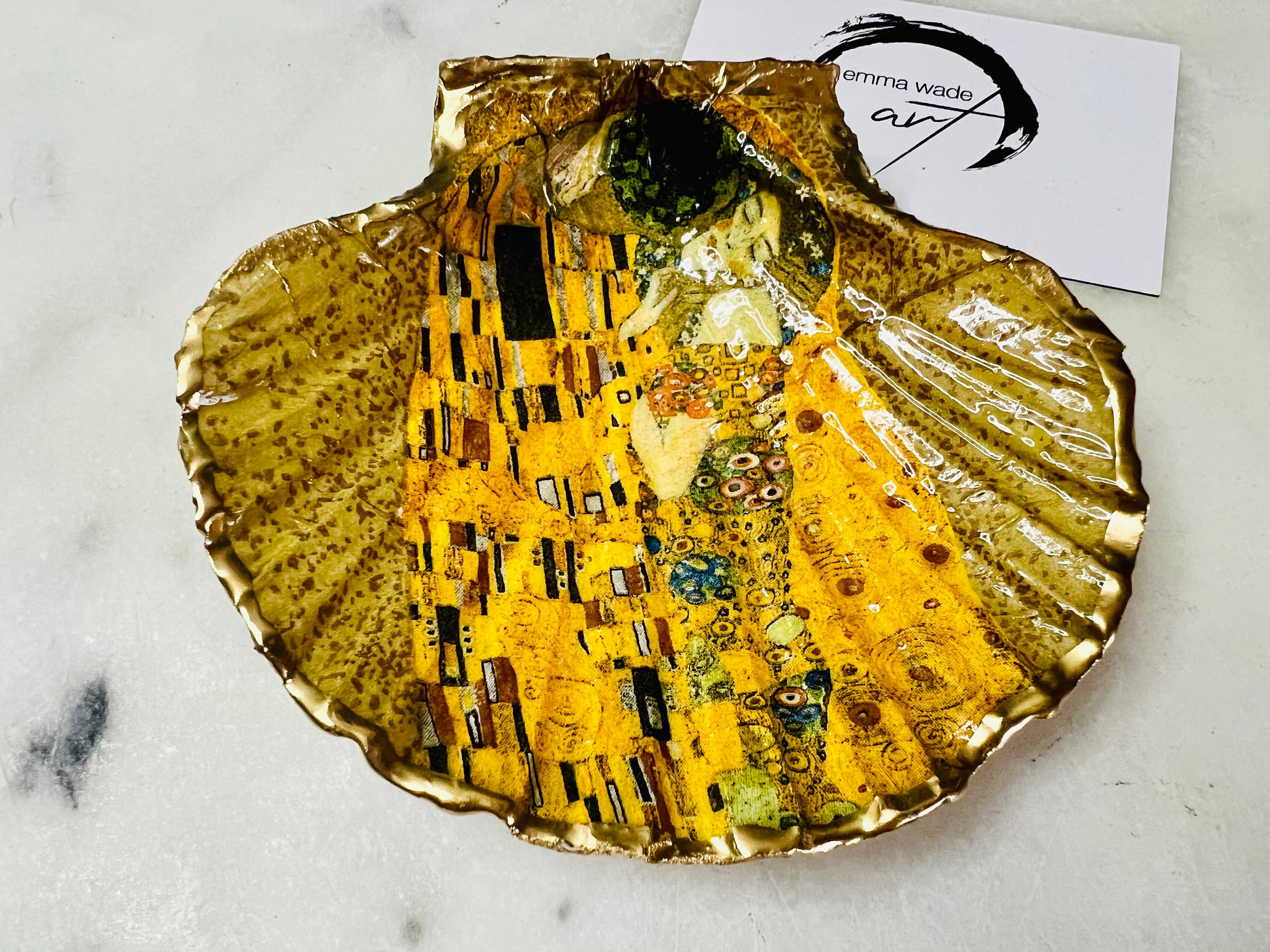 Handmade scallop shell trinket dish inspired by Gustav Klimt’s “The Kiss”, finished with gold leaf and sealed with glossy resin. Coastal Dorset shell jewellery dish perfect for rings, earrings and small treasures. Unique decorative shell bowl with golden artwork design, photographed on a light background showing detailed gilded surface and natural shell shape.
