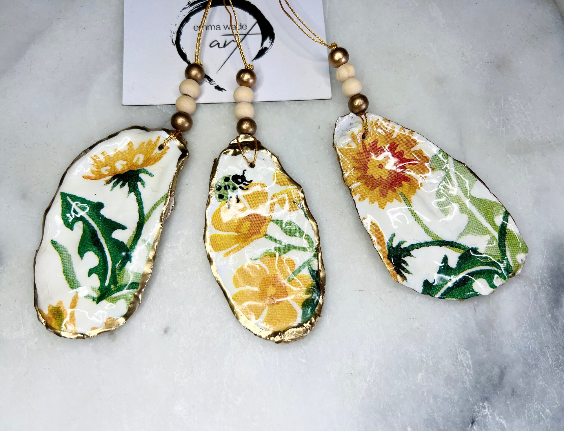Handmade Dorset oyster shell hanging ornament featuring genuine Emma Bridgewater yellow spring floral napkin design, finished with gold leaf edging and glossy resin. Natural pearlescent reverse with gold detailing and gold hanging cord with decorative beads. Coastal seasonal home decor.