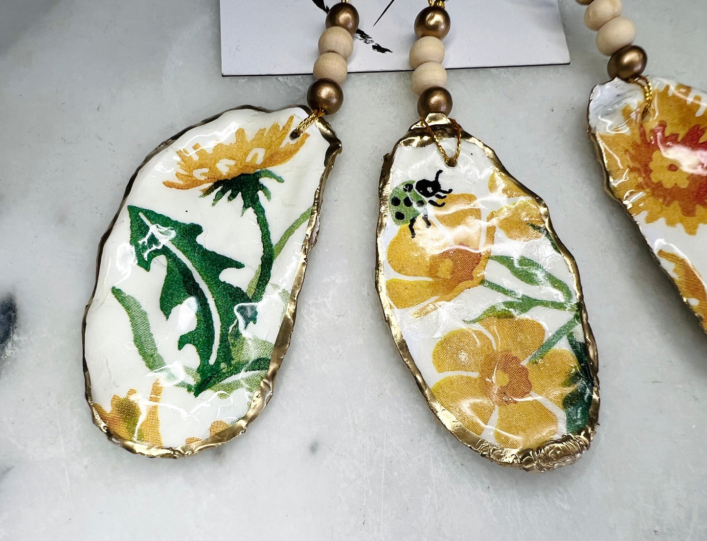 Handmade Dorset oyster shell hanging ornament featuring genuine Emma Bridgewater yellow spring floral napkin design, finished with gold leaf edging and glossy resin. Natural pearlescent reverse with gold detailing and gold hanging cord with decorative beads. Coastal seasonal home decor.