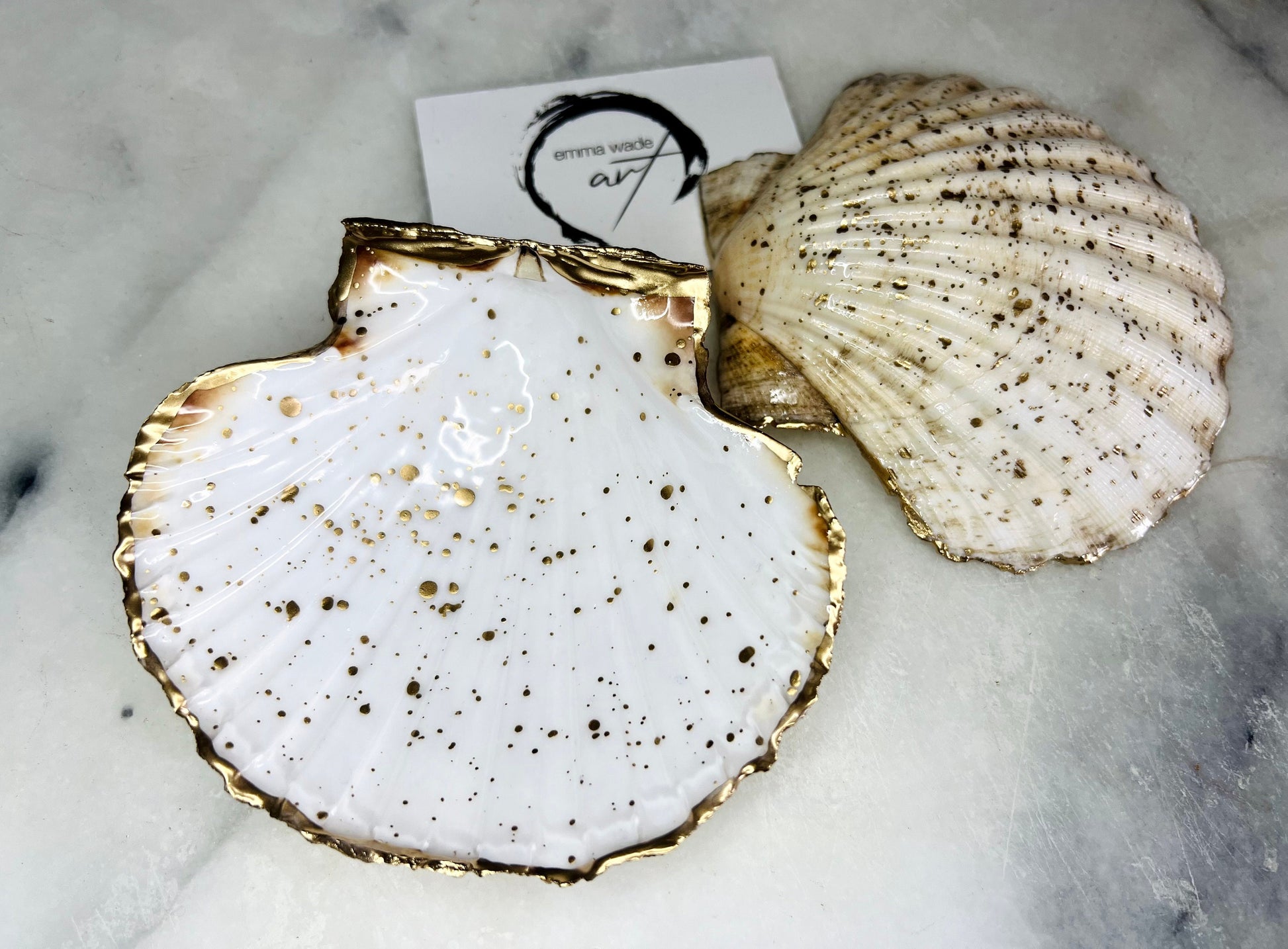Handmade Dorset scallop shell trinket dishes featuring natural white shells with delicate liquid gold leaf speckling, hand-painted gold leaf edging and glossy crystal clear resin. Luxury coastal jewellery dishes styled on a white marble background with elegant neutral tones and artisan coastal home décor styling.