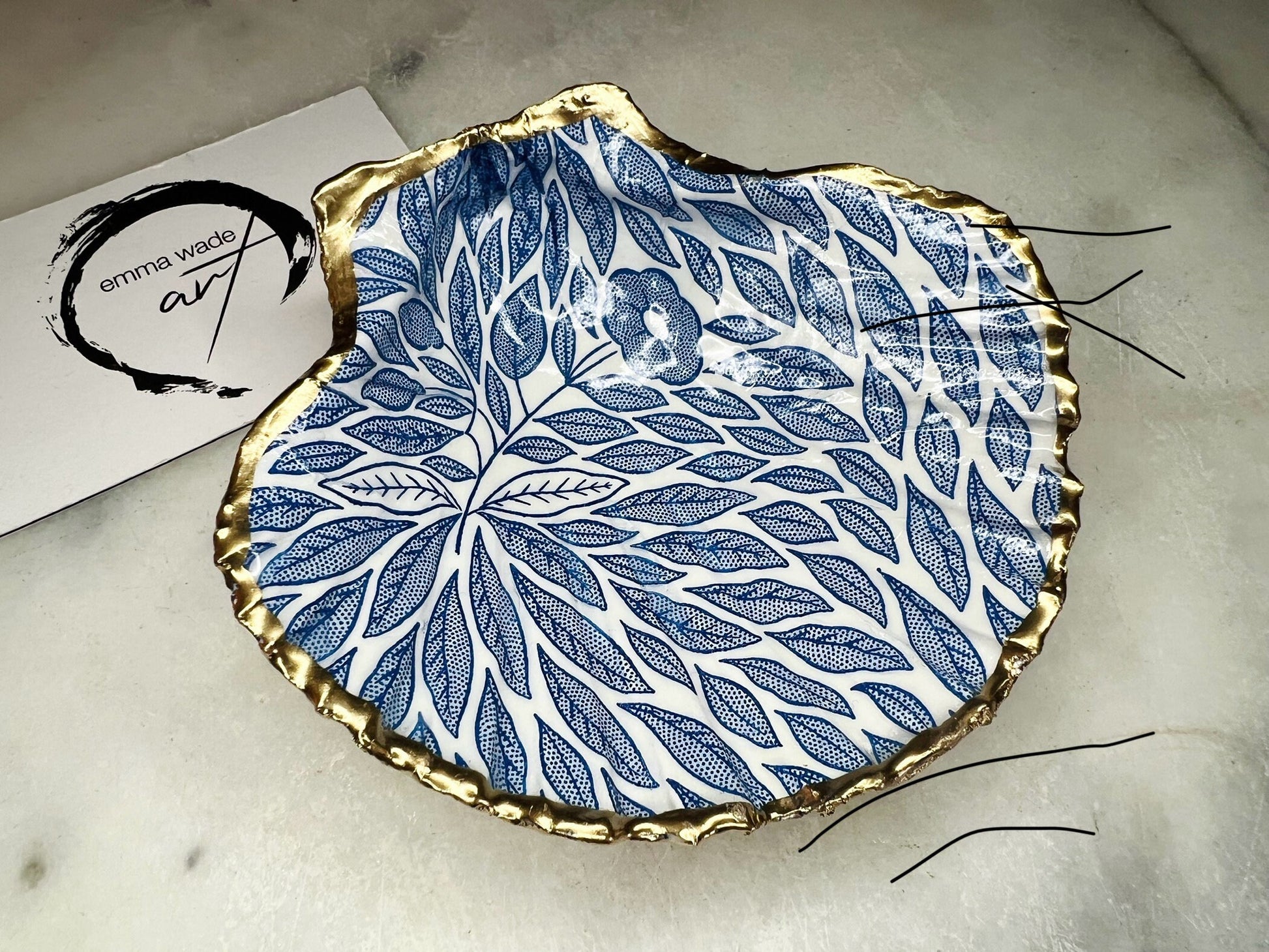 Handmade Dorset scallop shell trinket dishes featuring intricate blue floral and leaf artwork with hand-painted gold leaf edging and glossy crystal clear resin. Coastal botanical jewellery dishes inspired by Nordic Scandinavian decor, styled on a neutral background with elegant blue flower detailing and gilded edges.