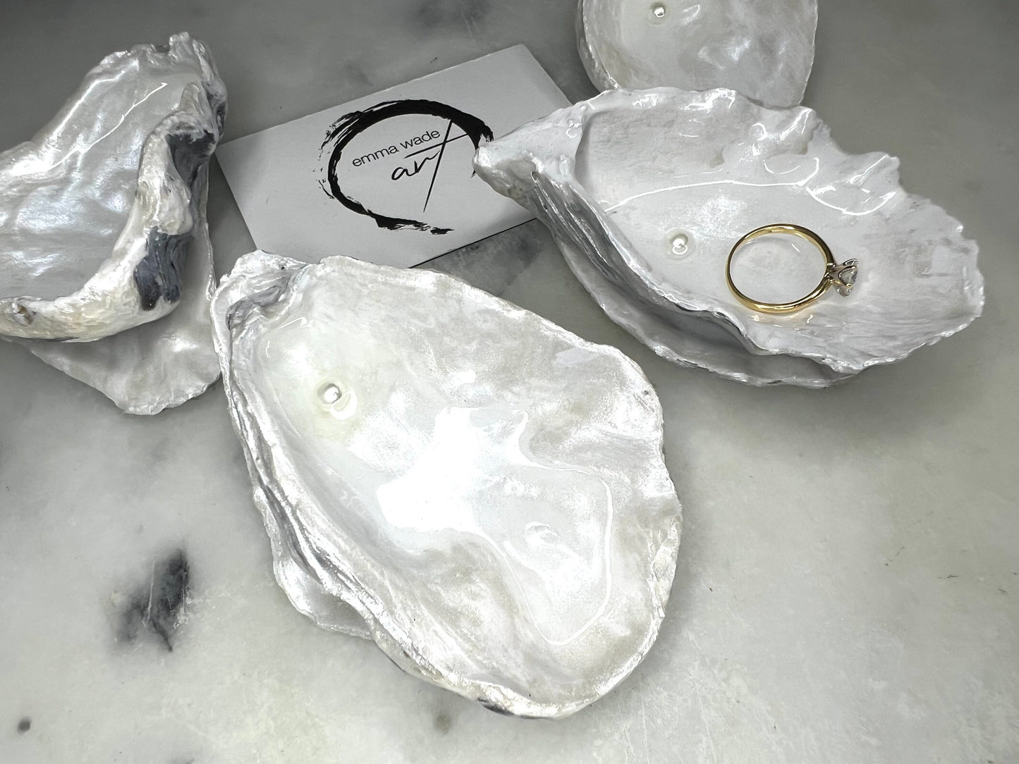 Handcrafted Dorset oyster shell ring box with matching natural shell lid, featuring a luminous inset Swarovski pearl nestled inside the cupped shell. Interior has a soft pearlescent white sheen and is sealed with crystal-clear resin. Optional outer finish in natural pearl tone or pearl with subtle gold leaf highlights. Coastal-inspired engagement proposal ring holder and wedding keepsake, styled on marble surface.