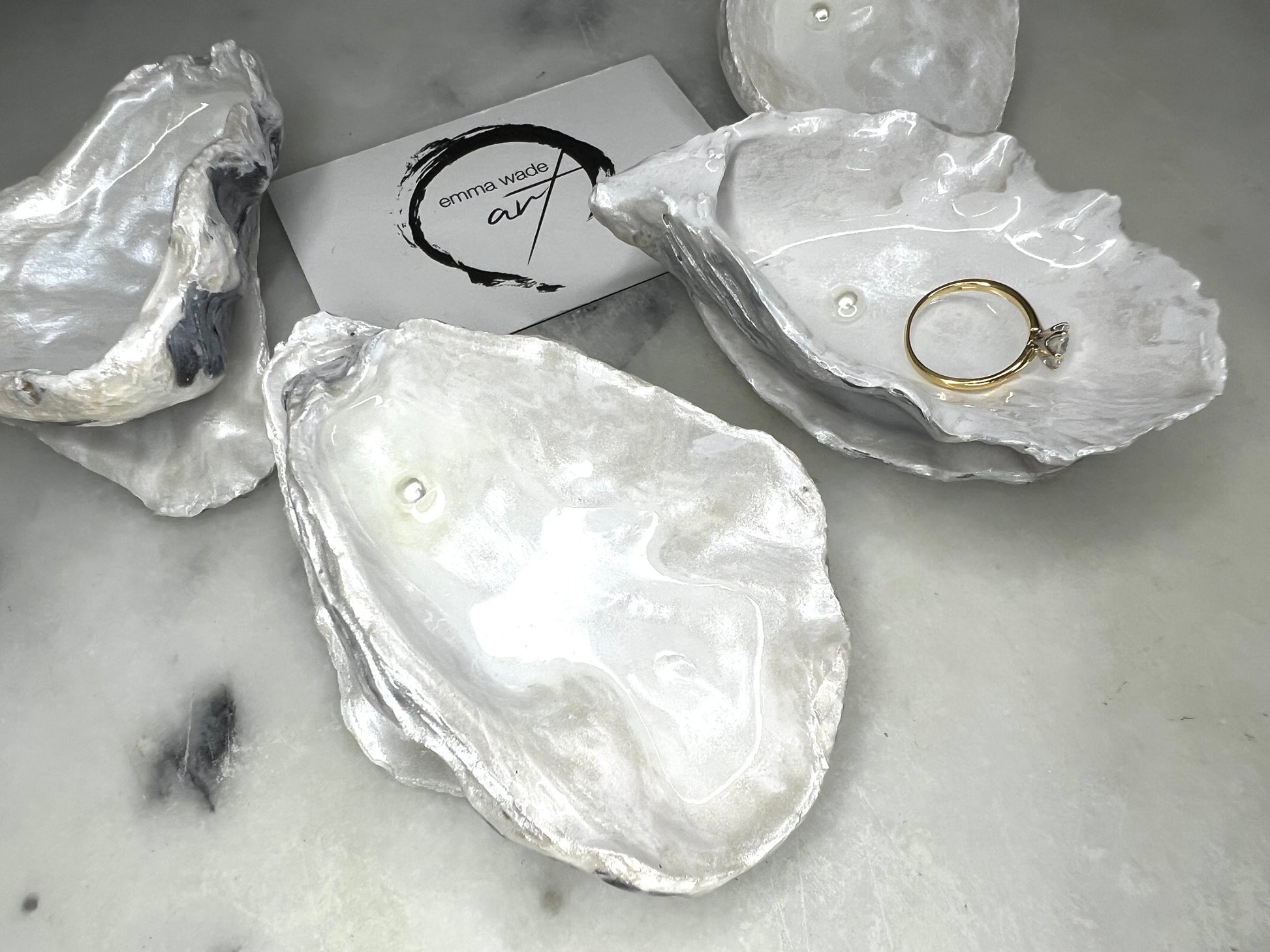 Handcrafted Dorset oyster shell ring box with matching natural shell lid, featuring a luminous inset Swarovski pearl nestled inside the cupped shell. Interior has a soft pearlescent white sheen and is sealed with crystal-clear resin. Optional outer finish in natural pearl tone or pearl with subtle gold leaf highlights. Coastal-inspired engagement proposal ring holder and wedding keepsake, styled on marble surface.