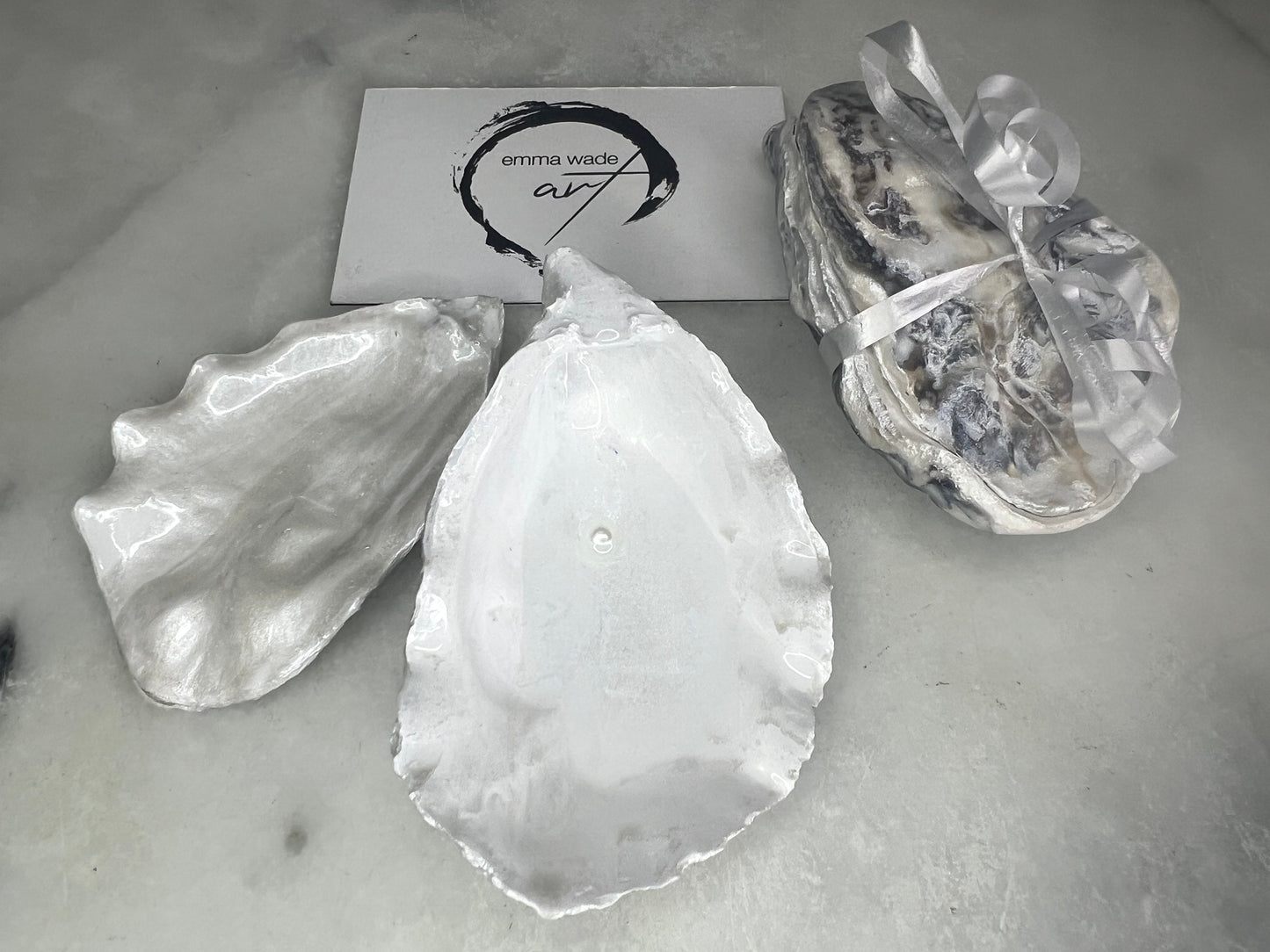 Handcrafted Dorset oyster shell ring box with matching natural shell lid, featuring a luminous inset Swarovski pearl nestled inside the cupped shell. Interior has a soft pearlescent white sheen and is sealed with crystal-clear resin. Optional outer finish in natural pearl tone or pearl with subtle gold leaf highlights. Coastal-inspired engagement proposal ring holder and wedding keepsake, styled on marble surface.