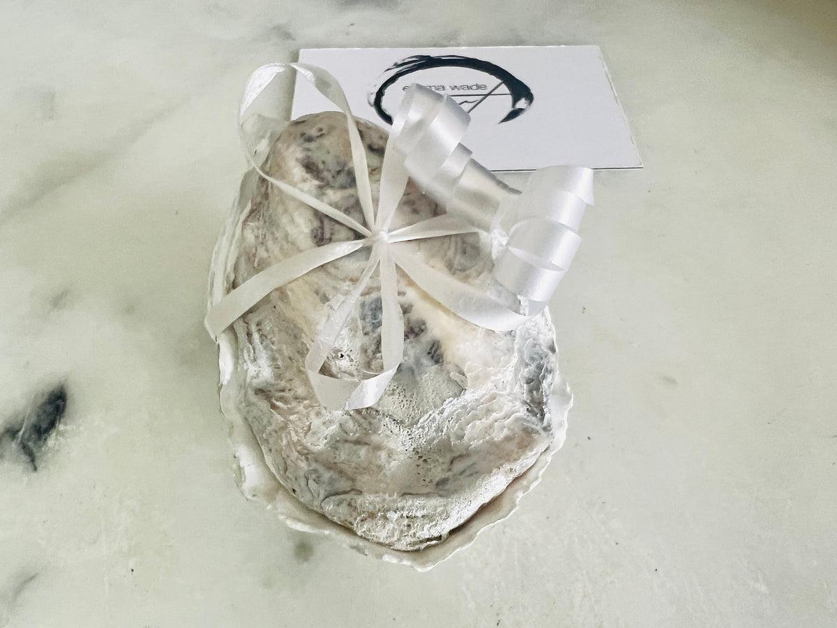 Handcrafted Dorset oyster shell ring box with matching natural shell lid, featuring a luminous inset Swarovski pearl nestled inside the cupped shell. Interior has a soft pearlescent white sheen and is sealed with crystal-clear resin. Optional outer finish in natural pearl tone or pearl with subtle gold leaf highlights. Coastal-inspired engagement proposal ring holder and wedding keepsake, styled on marble surface.