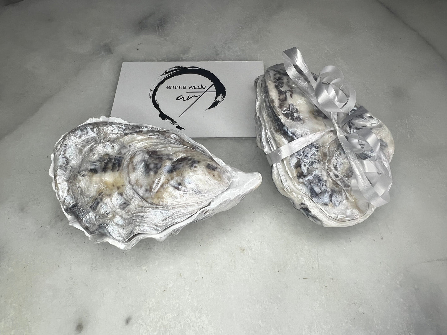 Handcrafted Dorset oyster shell ring box with matching natural shell lid, featuring a luminous inset Swarovski pearl nestled inside the cupped shell. Interior has a soft pearlescent white sheen and is sealed with crystal-clear resin. Optional outer finish in natural pearl tone or pearl with subtle gold leaf highlights. Coastal-inspired engagement proposal ring holder and wedding keepsake, styled on marble surface.