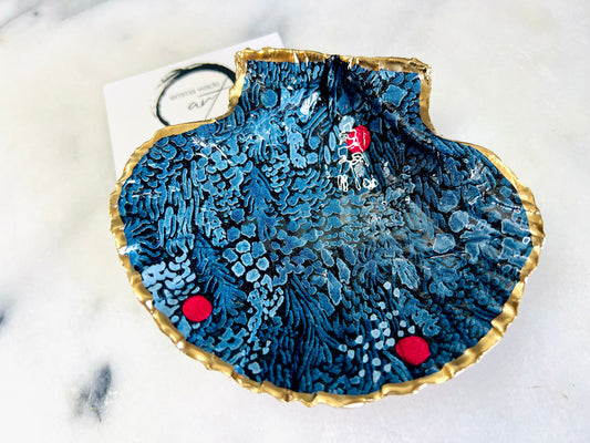 Handmade Marimekko inspired scallop shell trinket dish featuring bold Scandinavian floral design in deep blue with red accents. Natural Dorset scallop shell hand gilded with liquid gold leaf edging and sealed with glossy resin for a luxurious shine. Coastal home décor suitable as a jewellery dish, ring tray, trinket holder, wedding gift, bathroom décor or modern Nordic inspired shelf styling. Unique handcrafted shell décor inspired by botanical Scandinavian design.
