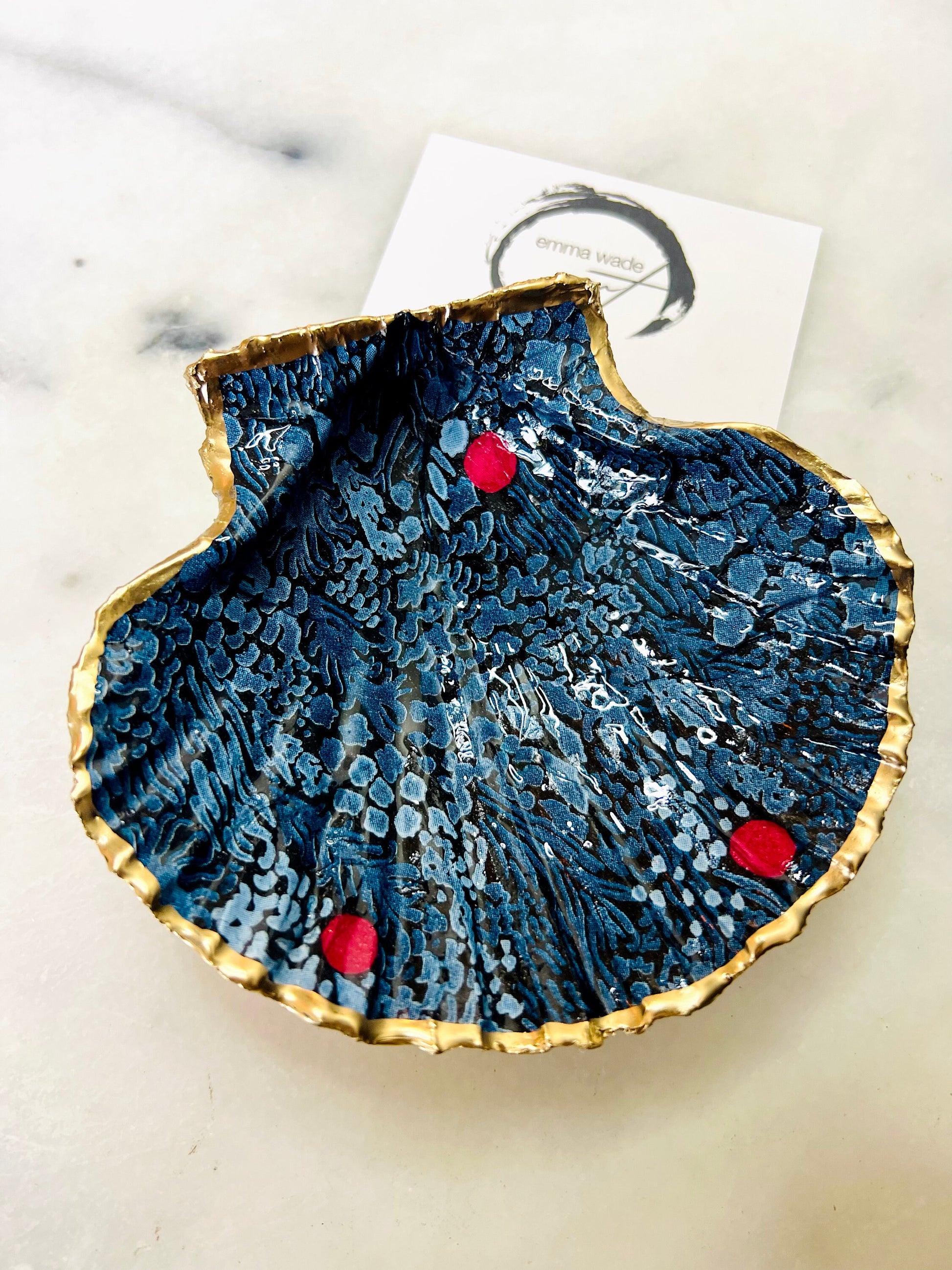 Handmade Marimekko inspired scallop shell trinket dish featuring bold Scandinavian floral design in deep blue with red accents. Natural Dorset scallop shell hand gilded with liquid gold leaf edging and sealed with glossy resin for a luxurious shine. Coastal home décor suitable as a jewellery dish, ring tray, trinket holder, wedding gift, bathroom décor or modern Nordic inspired shelf styling. Unique handcrafted shell décor inspired by botanical Scandinavian design.