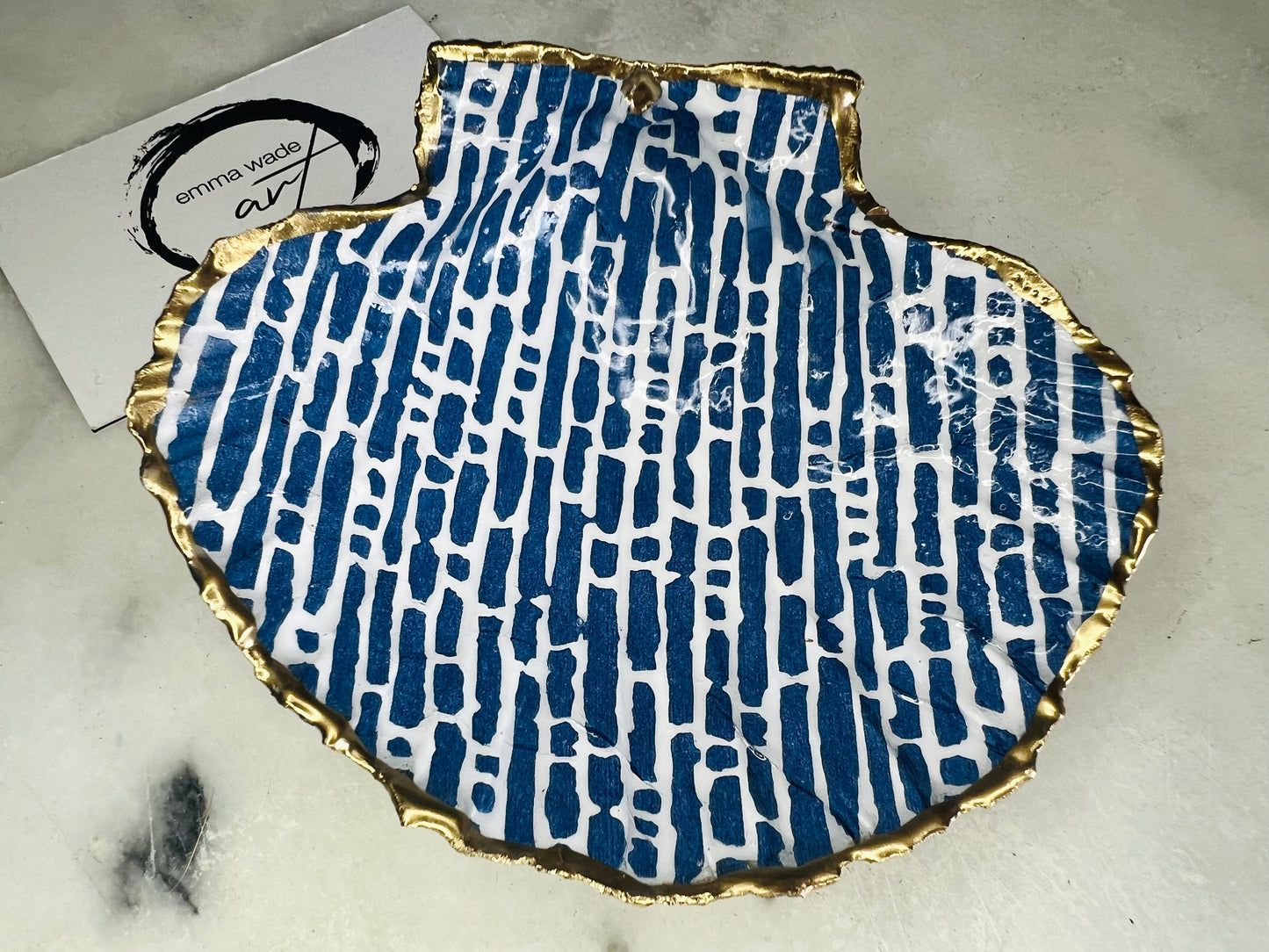 Handmade blue and white scallop shell trinket dish with gold leaf edging, crafted from a genuine Dorset shell and sealed with glossy resin. Coastal ring dish and jewellery holder featuring elegant blue line design, displayed in gift packaging. Artisan shell decor handmade in Surrey, perfect for coastal home styling, wedding gifts or nautical themed interiors.