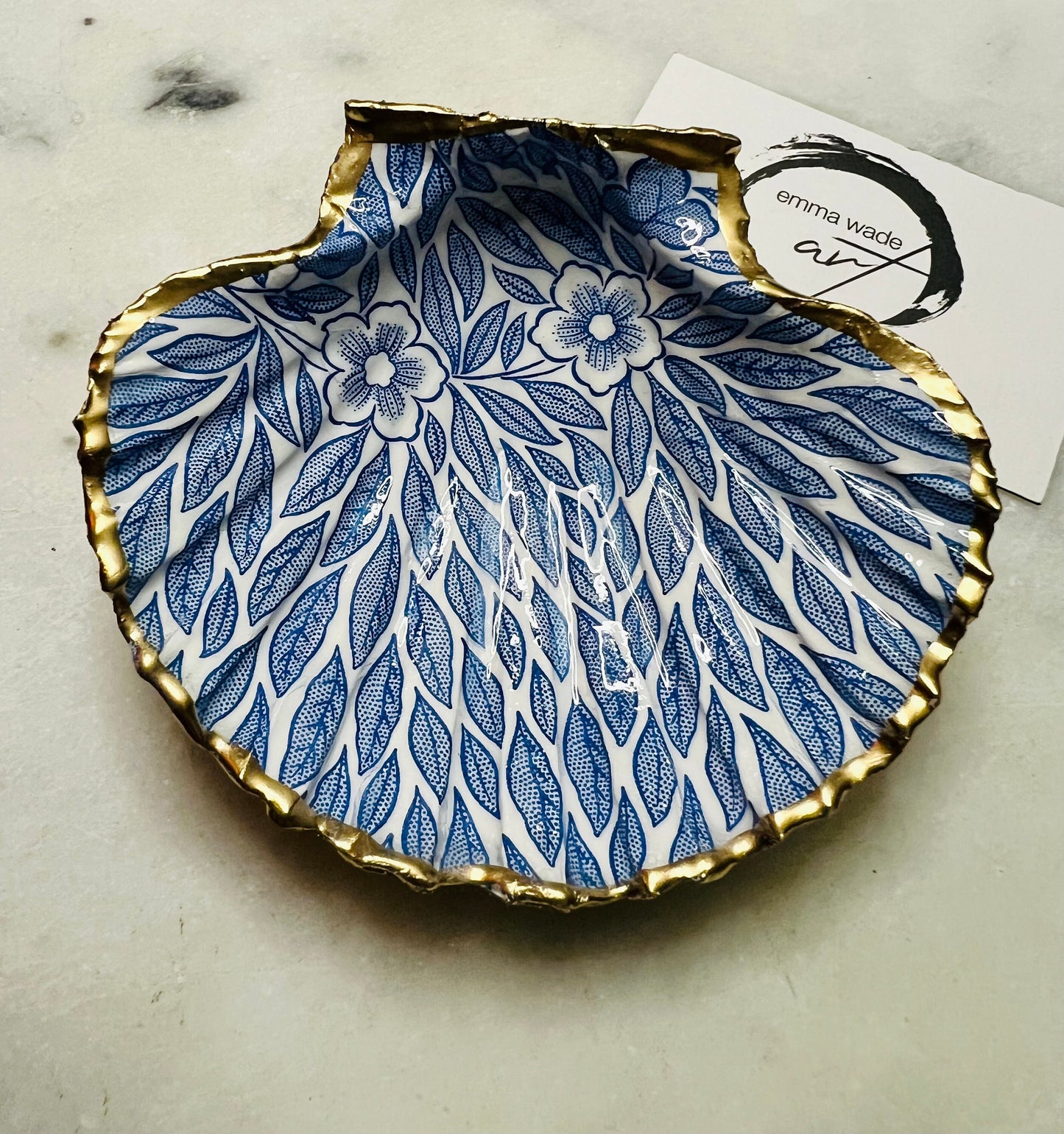 Handmade Dorset scallop shell trinket dishes featuring intricate blue floral and leaf artwork with hand-painted gold leaf edging and glossy crystal clear resin. Coastal botanical jewellery dishes inspired by Nordic Scandinavian decor, styled on a neutral background with elegant blue flower detailing and gilded edges.