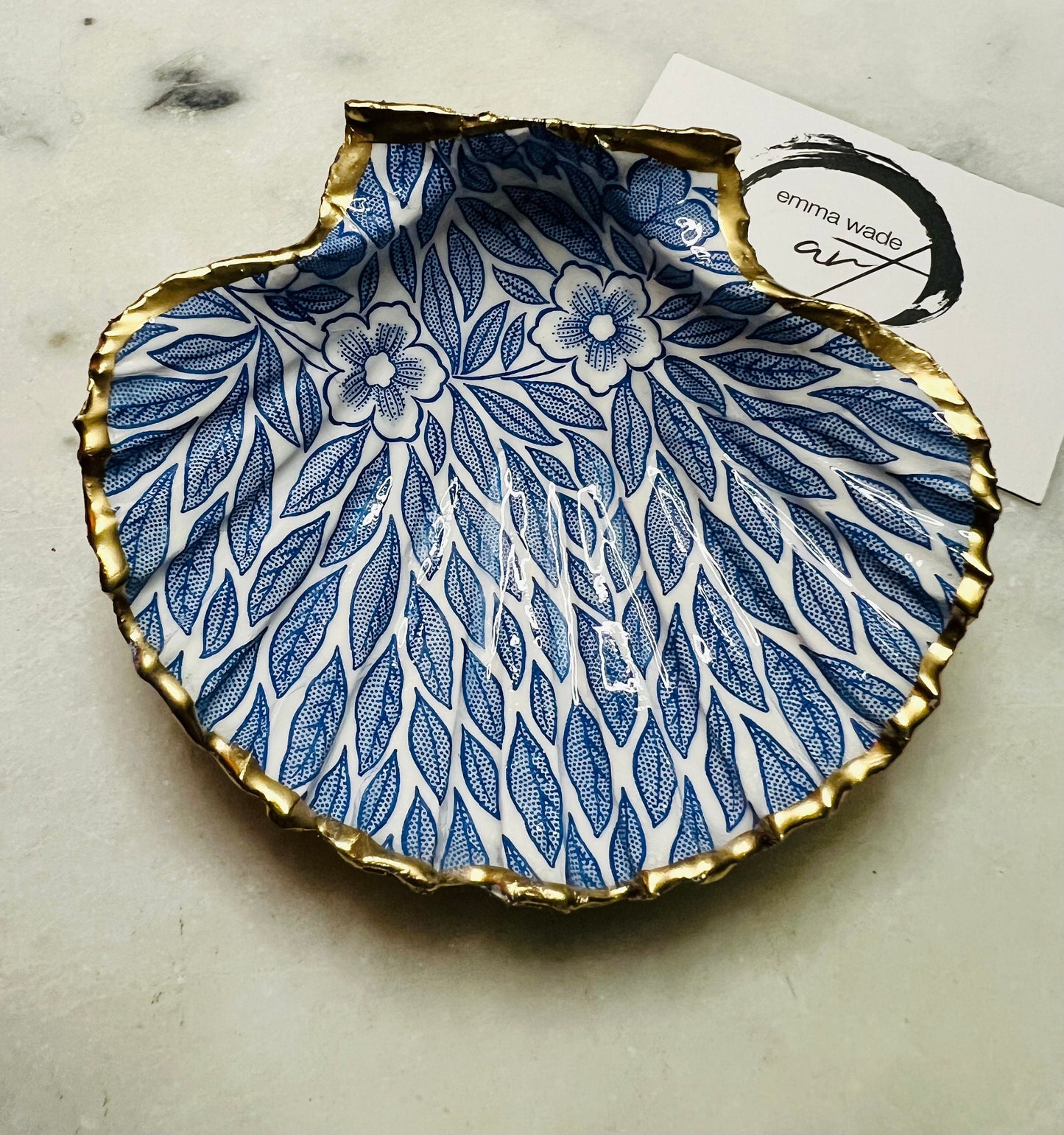 Handmade Dorset scallop shell trinket dishes featuring intricate blue floral and leaf artwork with hand-painted gold leaf edging and glossy crystal clear resin. Coastal botanical jewellery dishes inspired by Nordic Scandinavian decor, styled on a neutral background with elegant blue flower detailing and gilded edges.