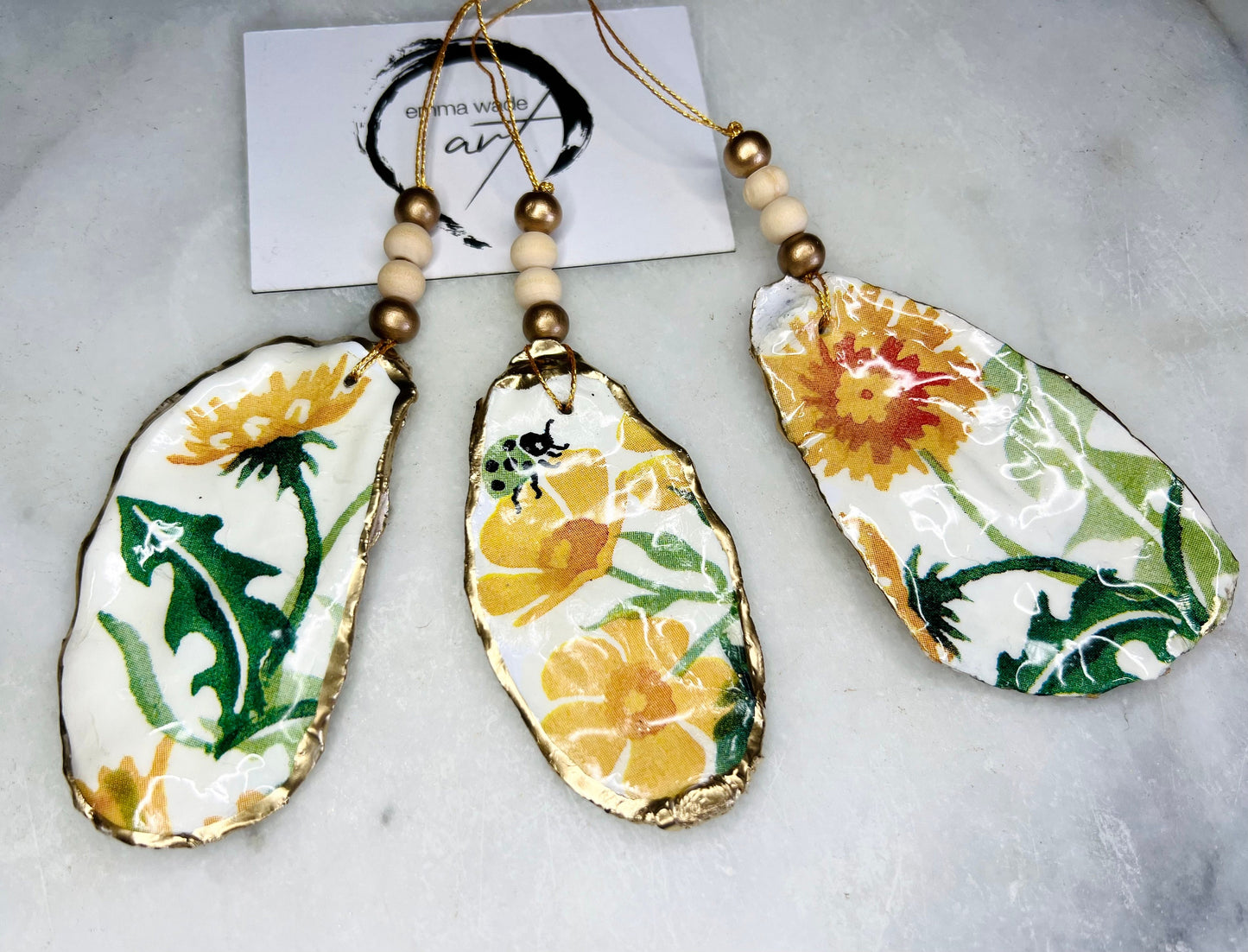 Handmade Dorset oyster shell hanging ornament featuring genuine Emma Bridgewater yellow spring floral napkin design, finished with gold leaf edging and glossy resin. Natural pearlescent reverse with gold detailing and gold hanging cord with decorative beads. Coastal seasonal home decor.